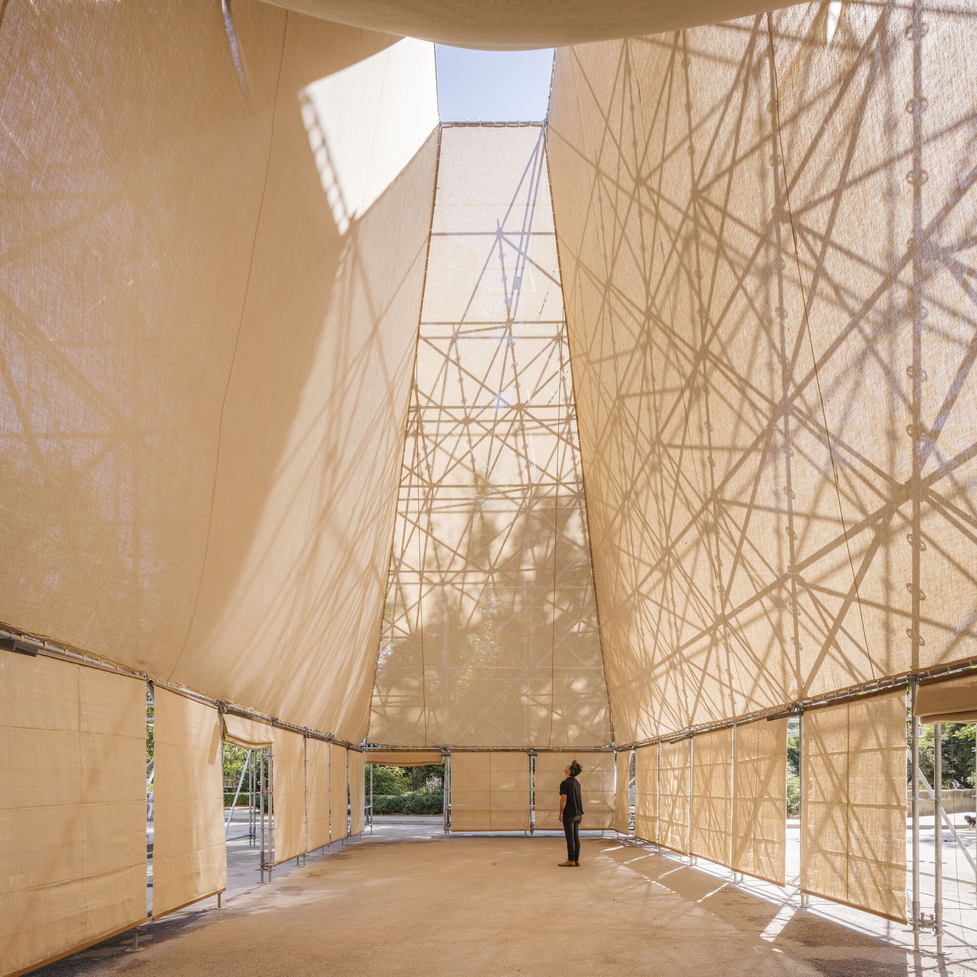 Interior view showing fabric-clad walls converging toward a square roof opening with a visitor standing inside