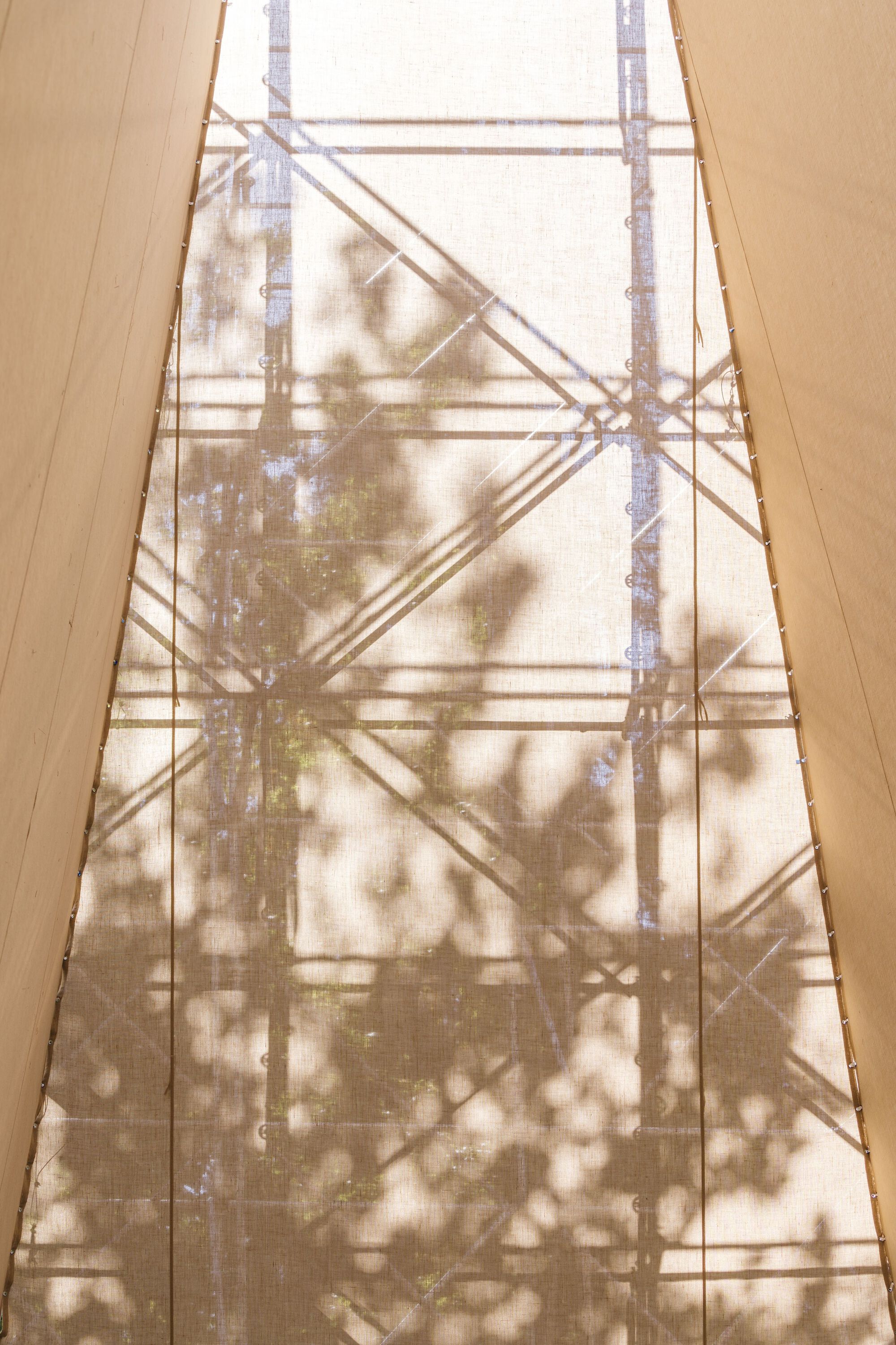 Scaffold shadows cast onto woven fabric panels illuminated by filtered daylight from above