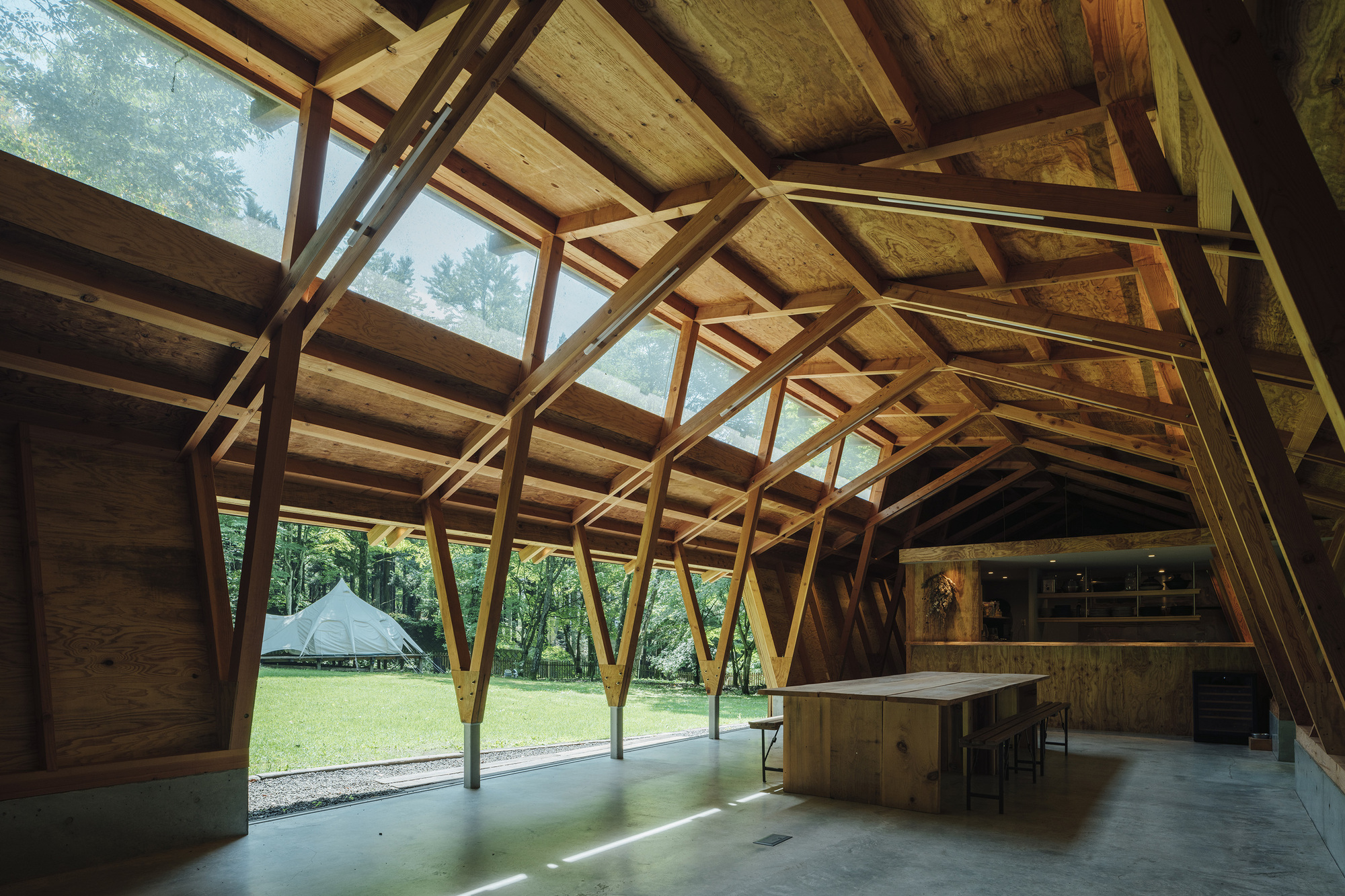 Interior space with exposed timber structure framing views to the green lawn and trees outside