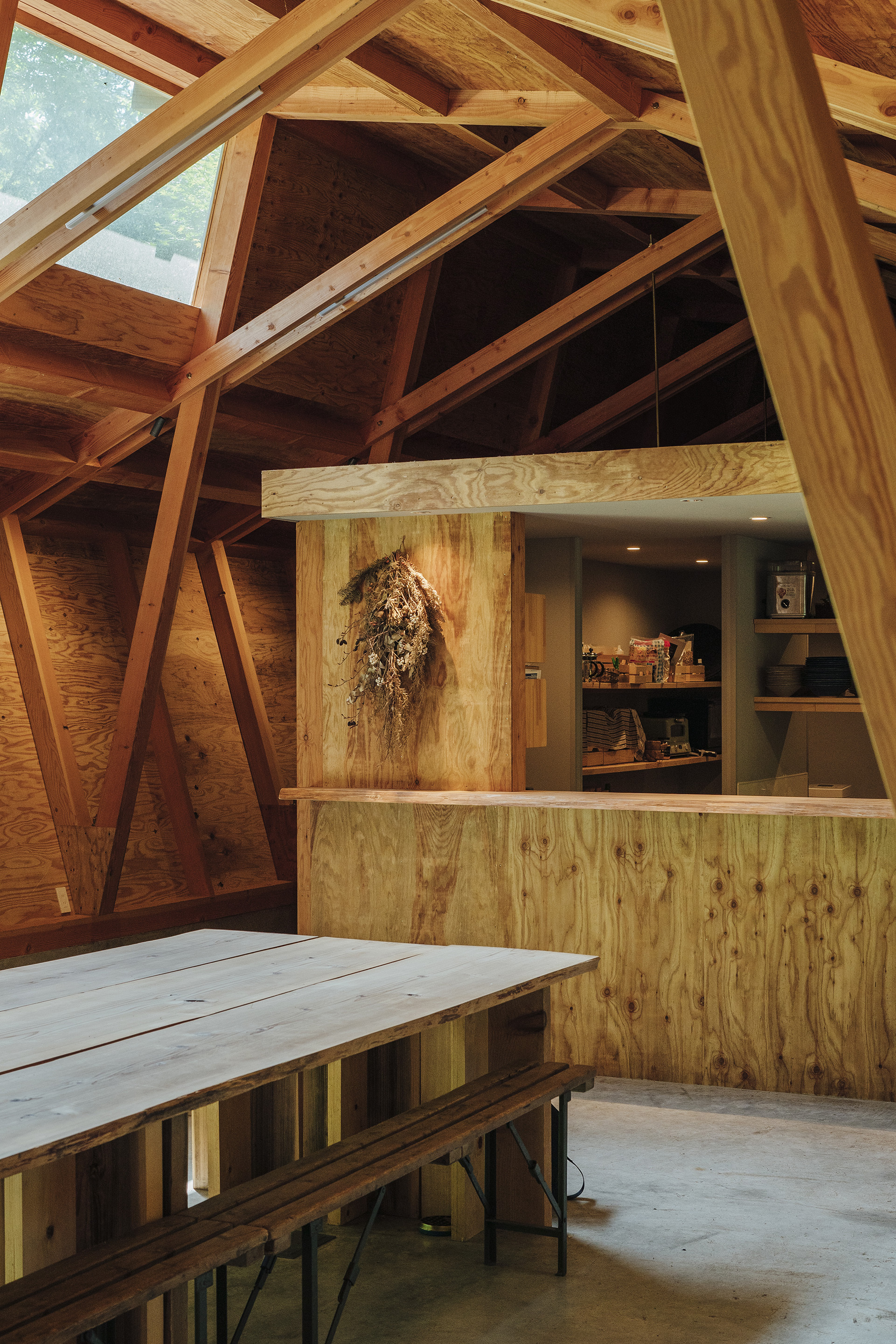 Plywood service counter beneath diagonal timber columns and exposed roof framing with dried flowers hanging on wall