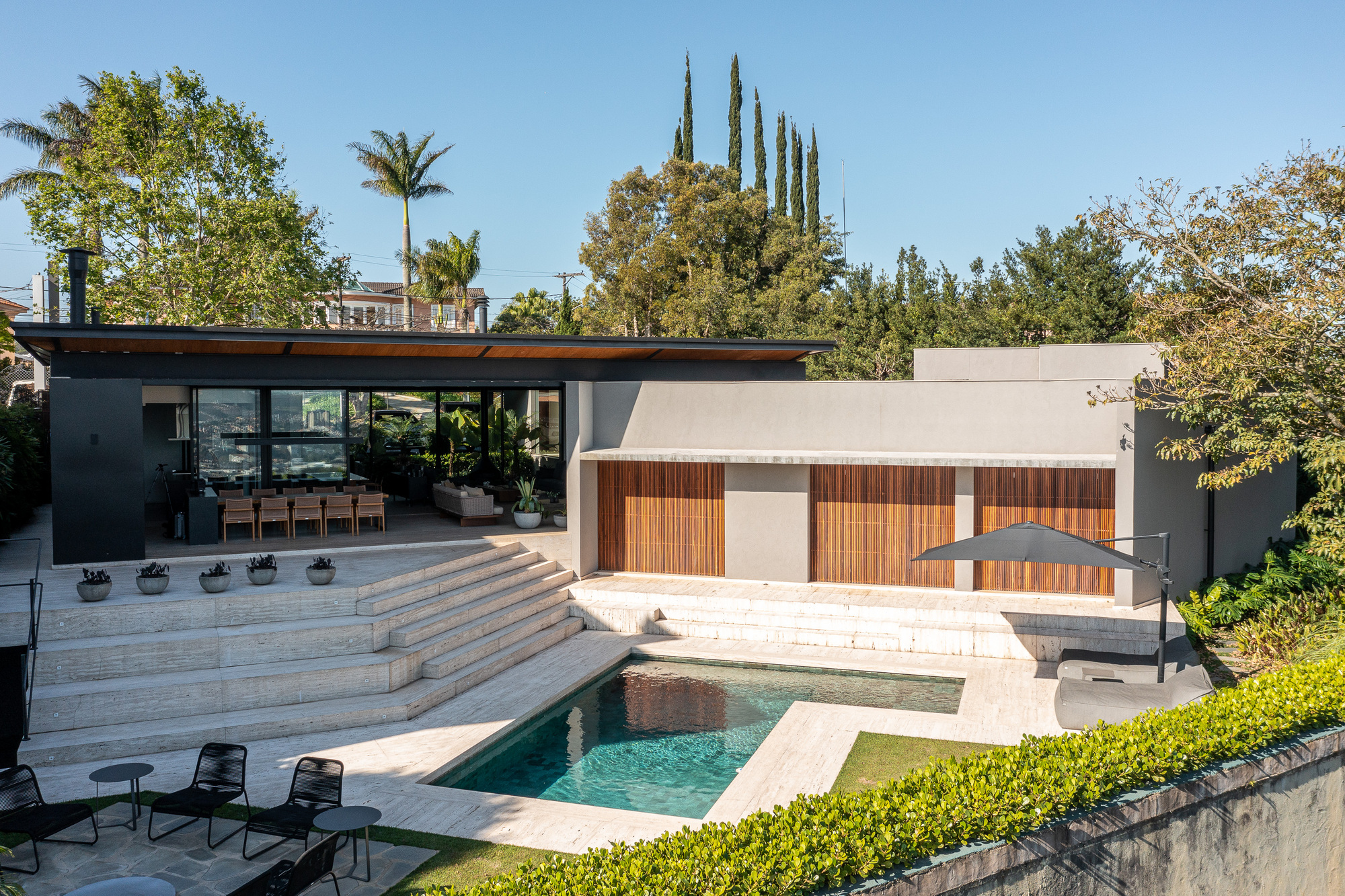 Rear courtyard with travertine pool deck and timber-clad volume framed by mature trees