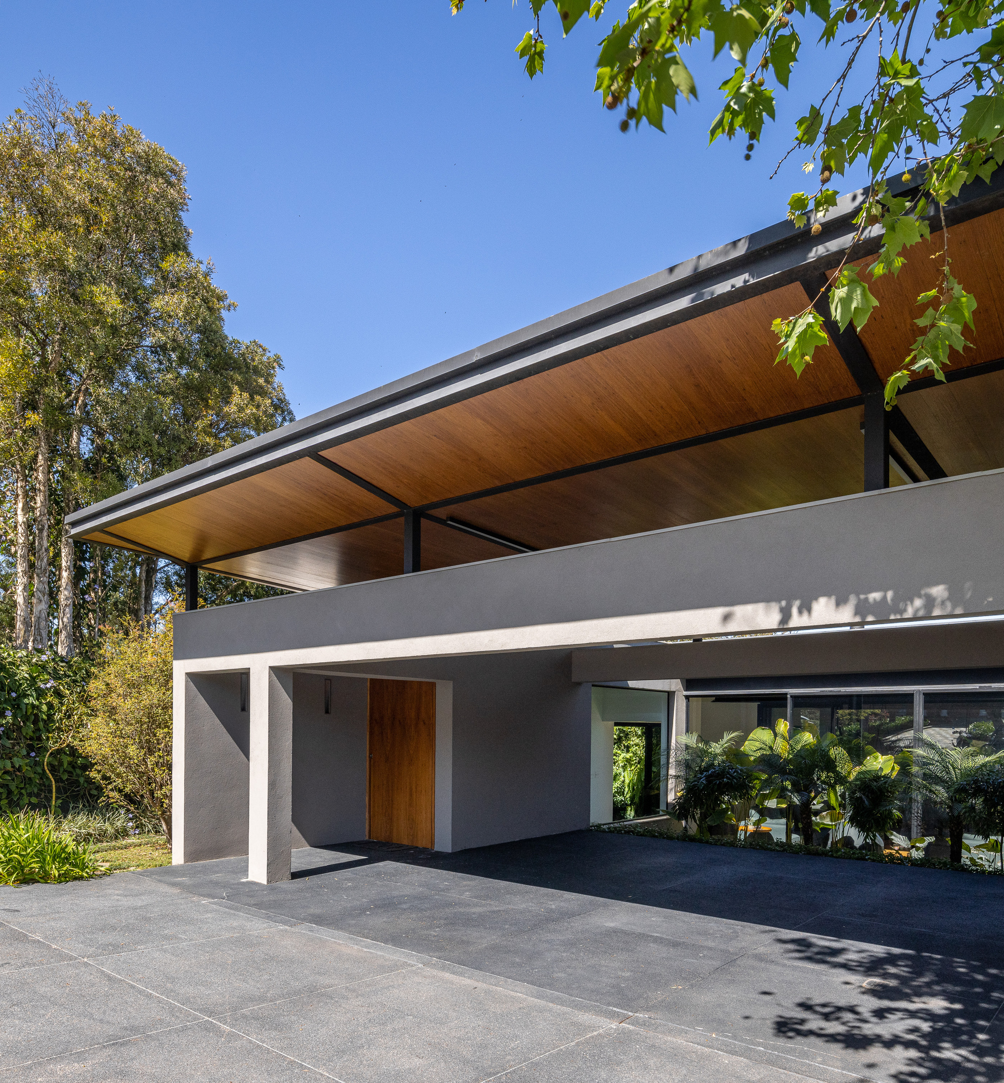 Entry canopy with exposed timber soffit and steel beams under dappled tree shade