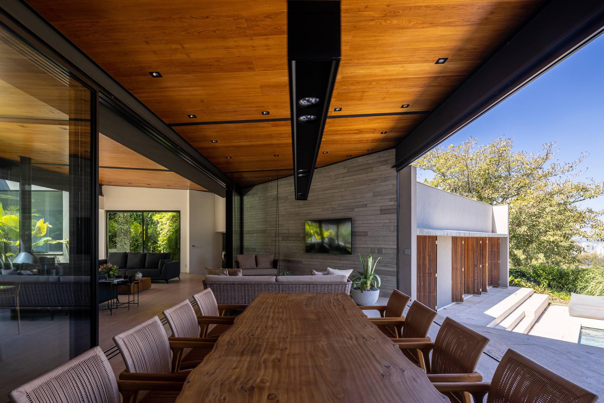 Covered terrace with long dining table, timber ceiling and grey brick fireplace wall