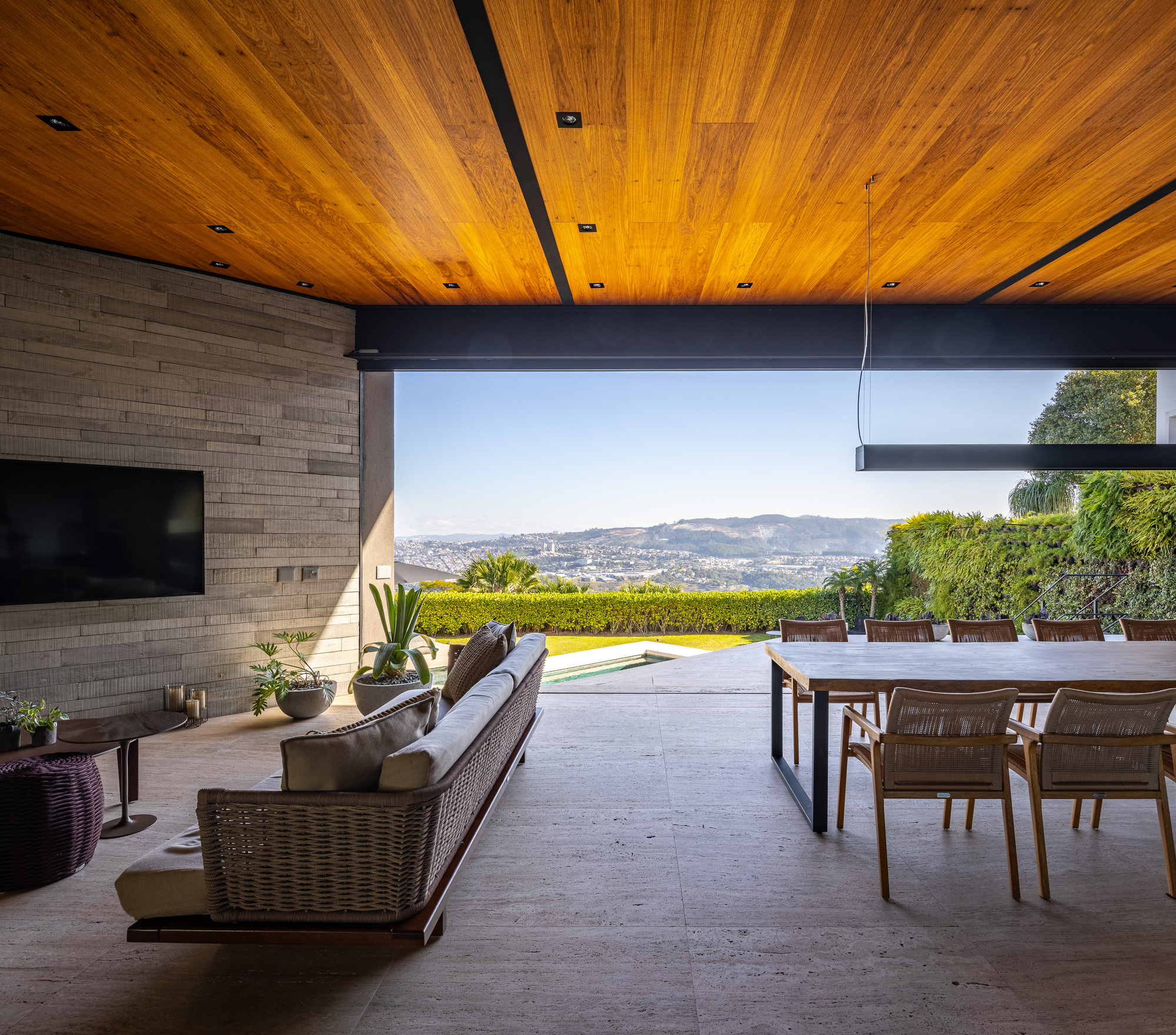 Outdoor living area with timber ceiling opening to hillside view beyond lawn and pool