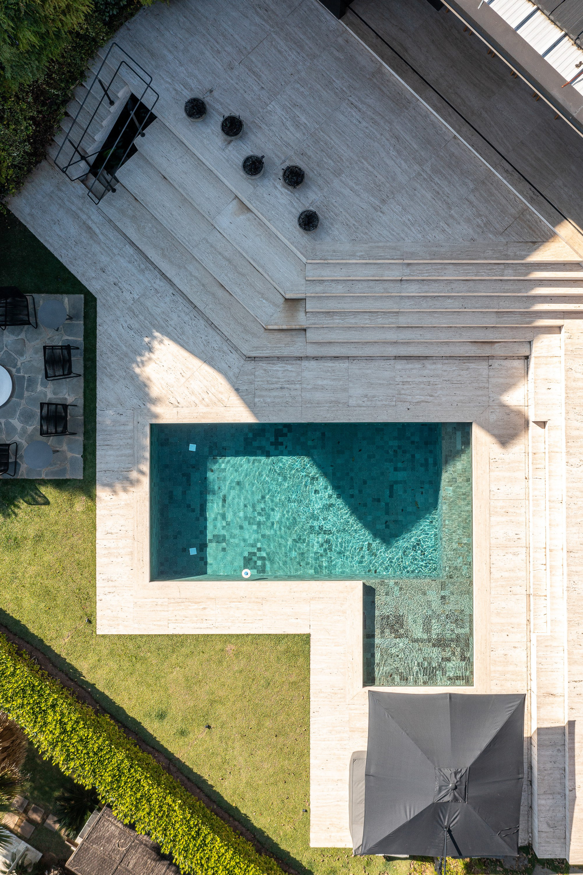 Aerial view of concrete deck with swimming pool and lawn courtyard in afternoon sunlight