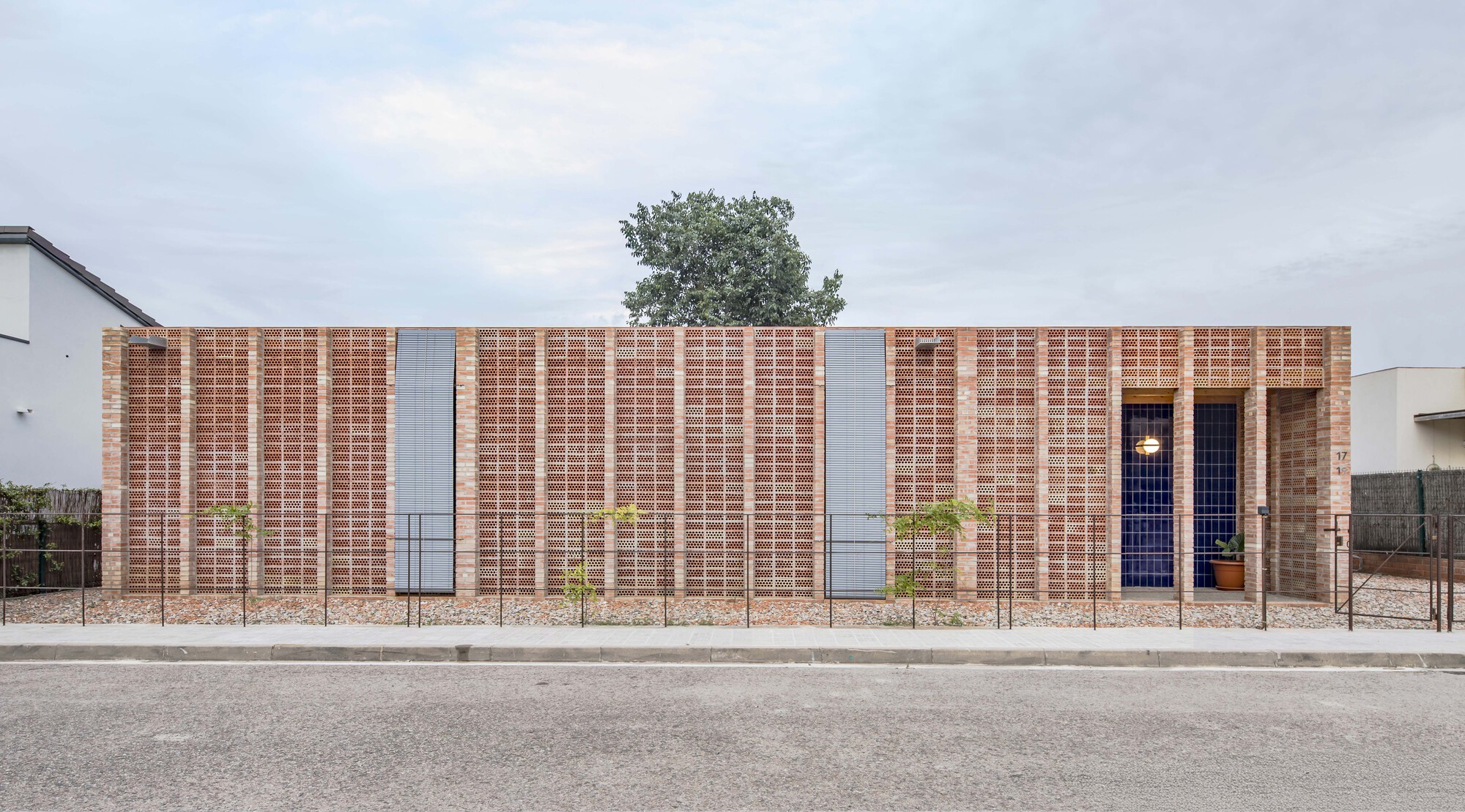 Street view of the perforated brick facade with vertical banding and a tree emerging from the roofline