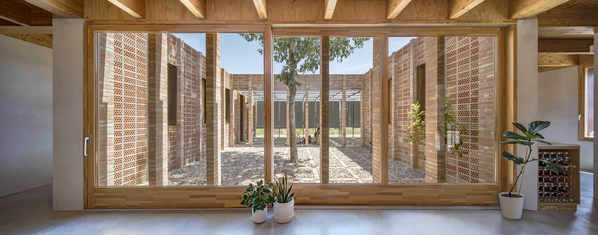 Timber-framed glazing overlooking a curved courtyard enclosed by perforated brick walls and gravel