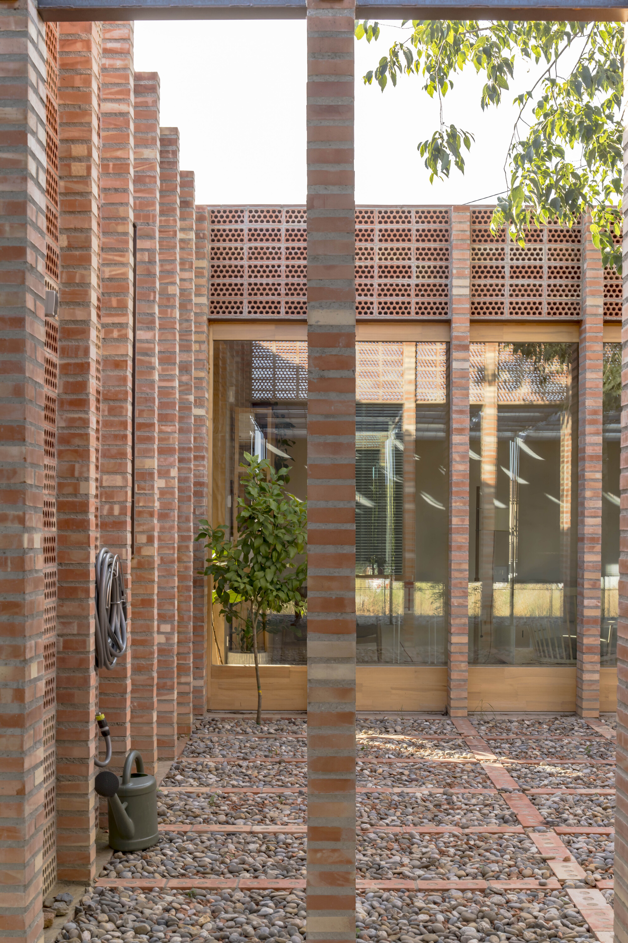 View through perforated brick columns into a courtyard with gravel and glazed doors