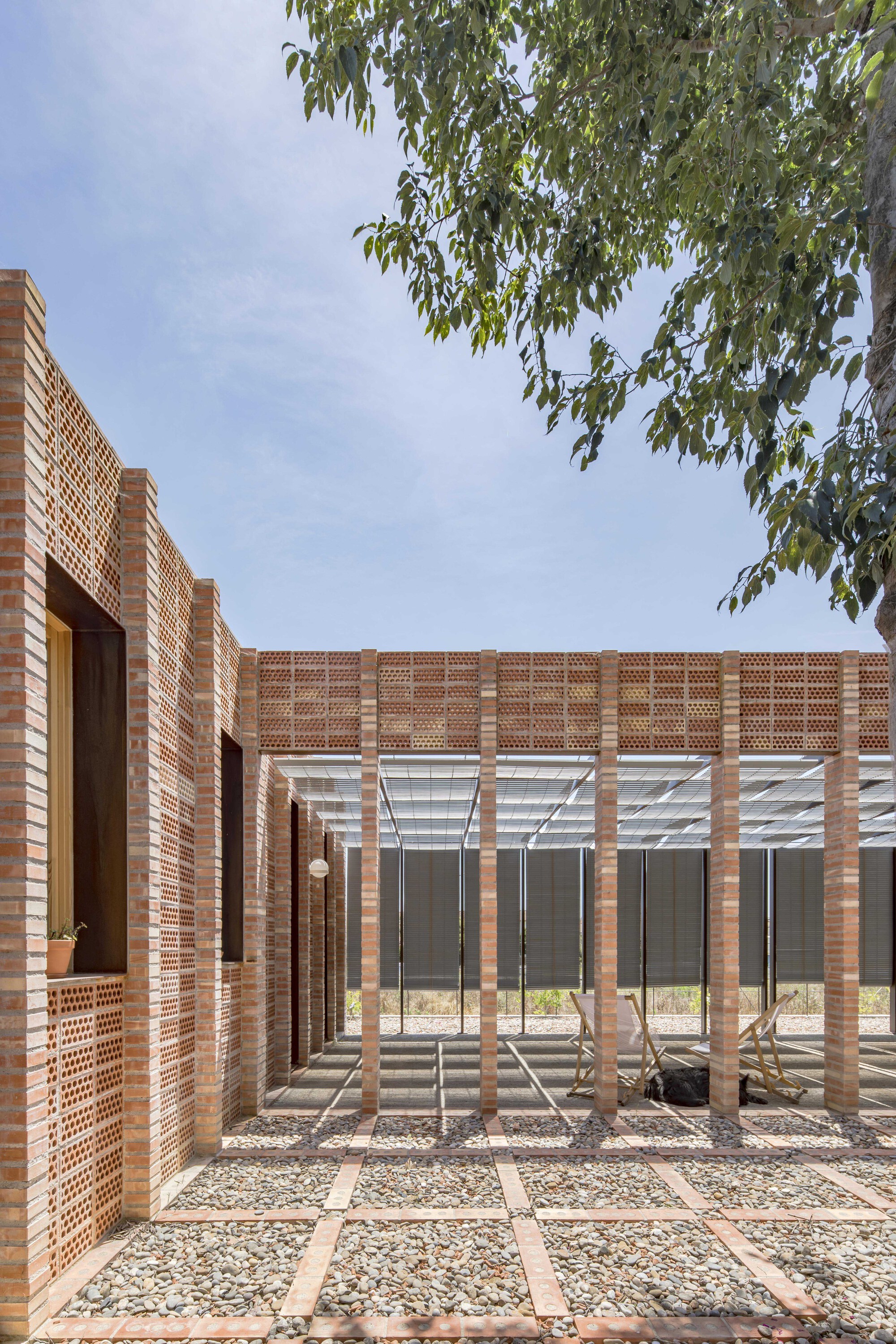 Courtyard with brick pergola columns and gravel grid pathways beneath tree branches overhead