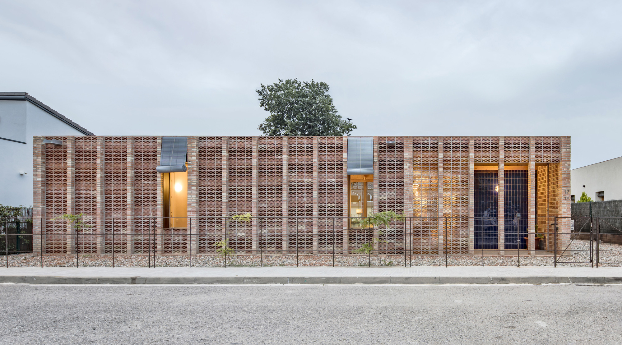 Street facade with layered brick walls and illuminated window openings at dusk
