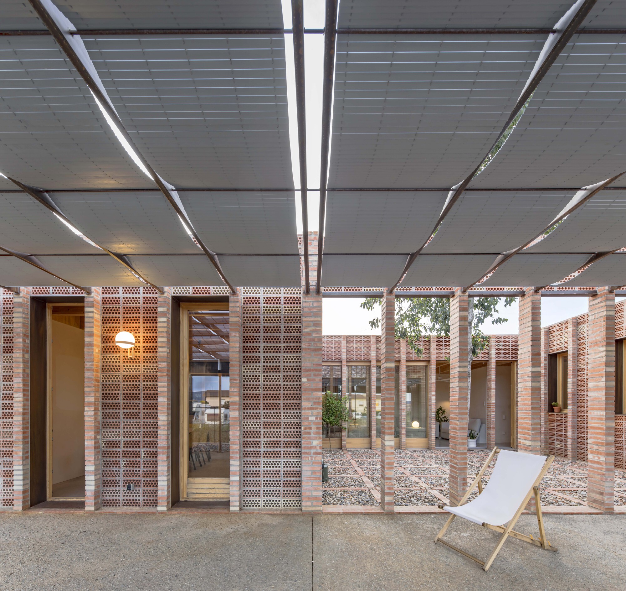 Covered porch with steel louvered canopy framing views of interior courtyard and perforated brick walls