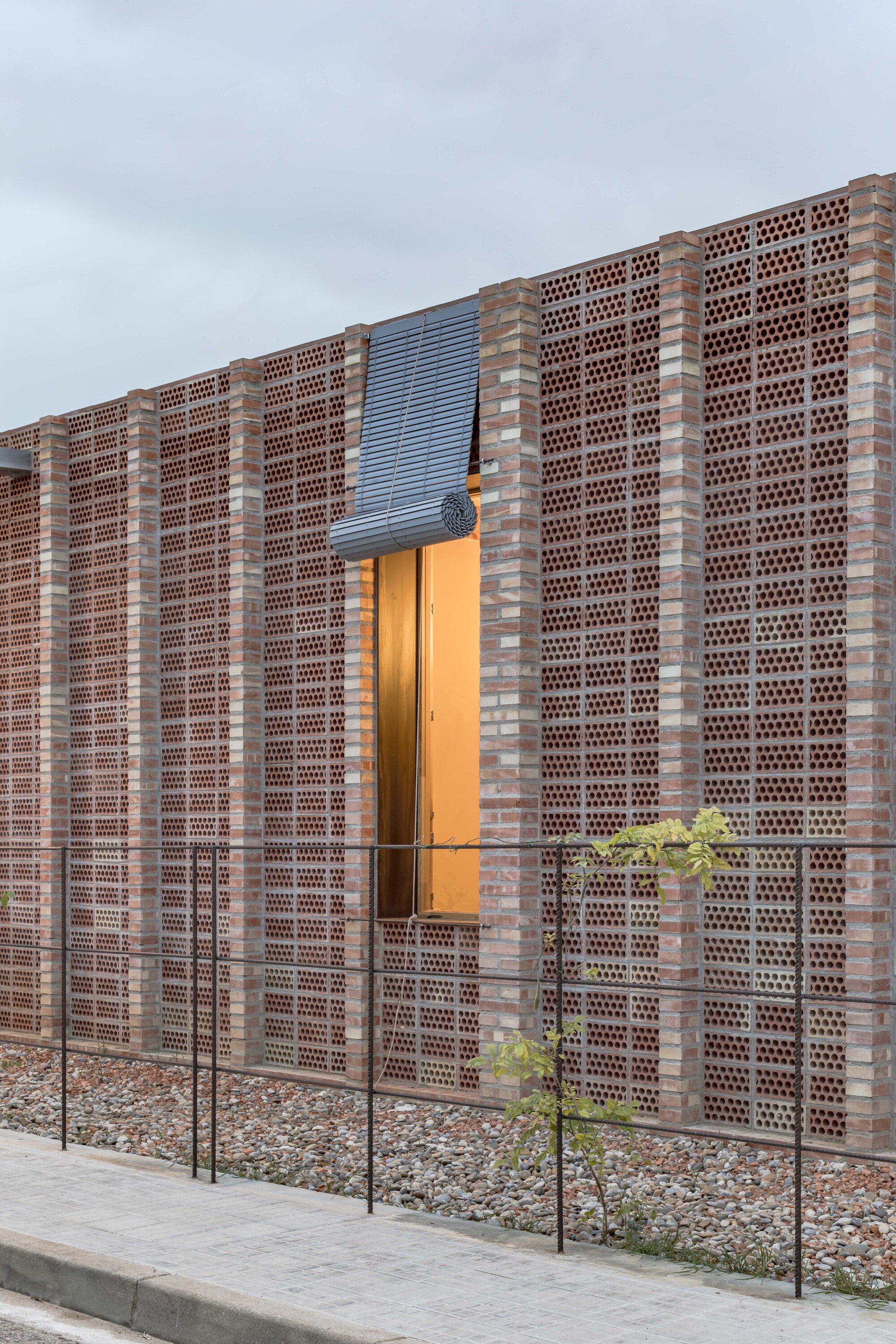 Corner detail of perforated brick wall with steel mesh panel and illuminated doorway at twilight