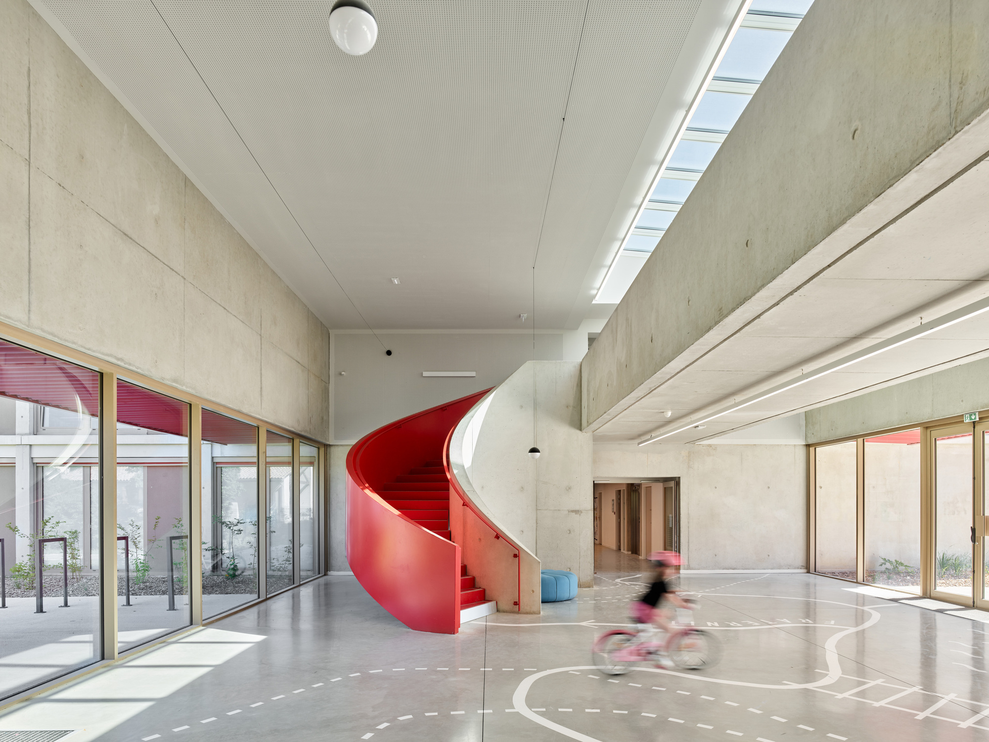 Red helical staircase connecting floors beside full-height glazing and concrete wall surfaces