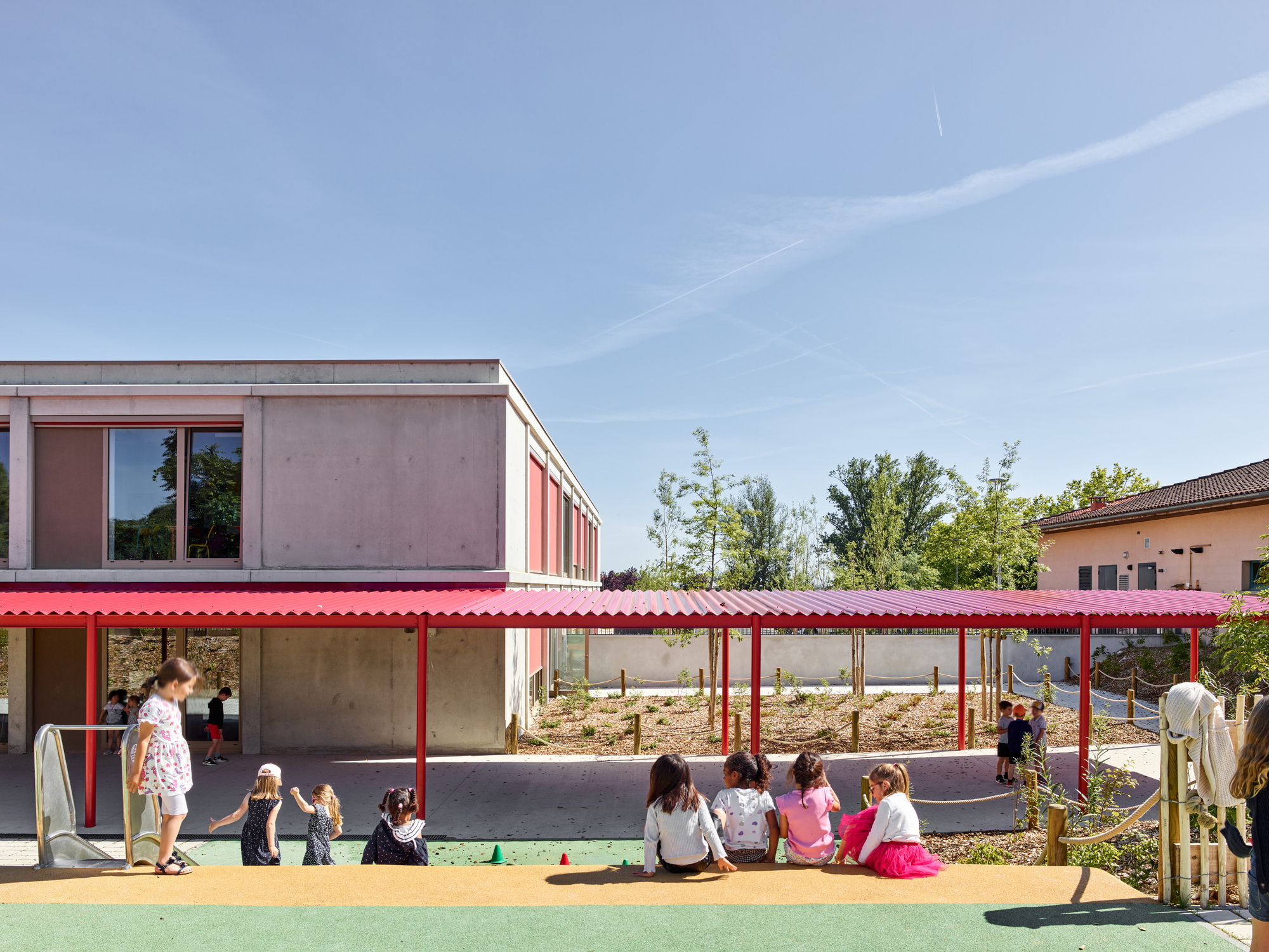 Outdoor play area with red canopy and children seated near a climbing mound under blue sky