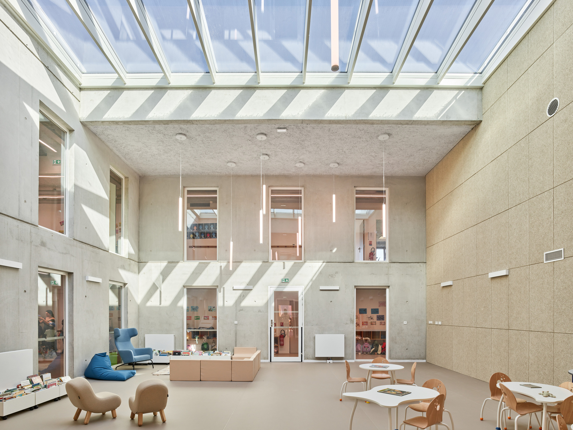 Double-height atrium with skylight roof and timber furniture scattered across the pale floor below