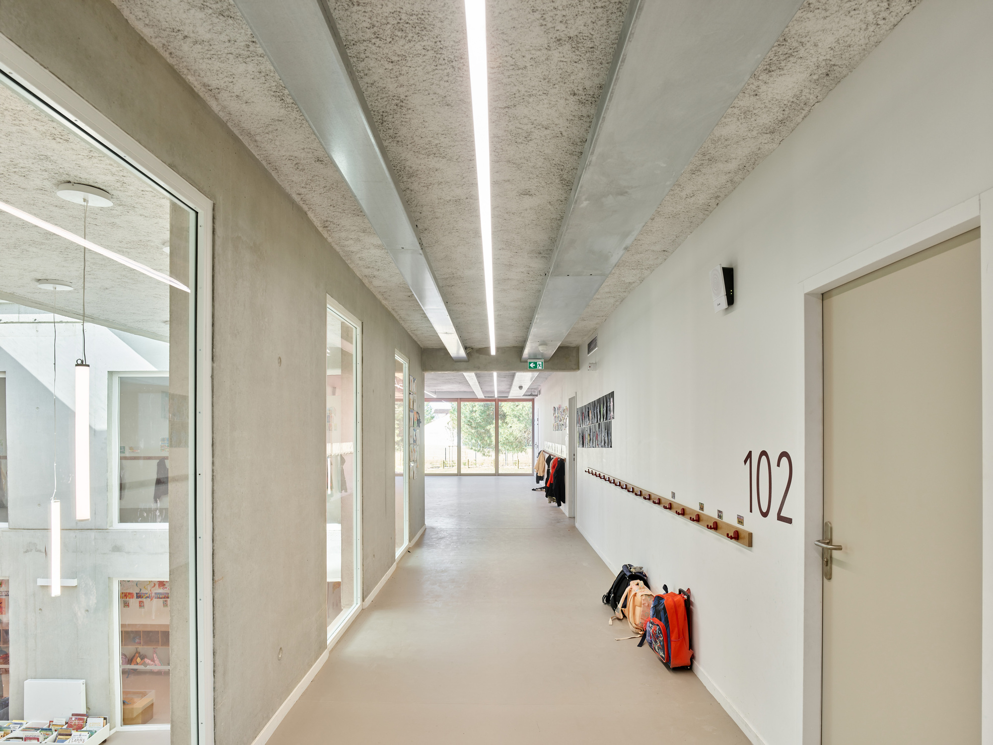 Upper-level corridor with glazed balustrade overlooking the atrium and coat hooks along the white wall