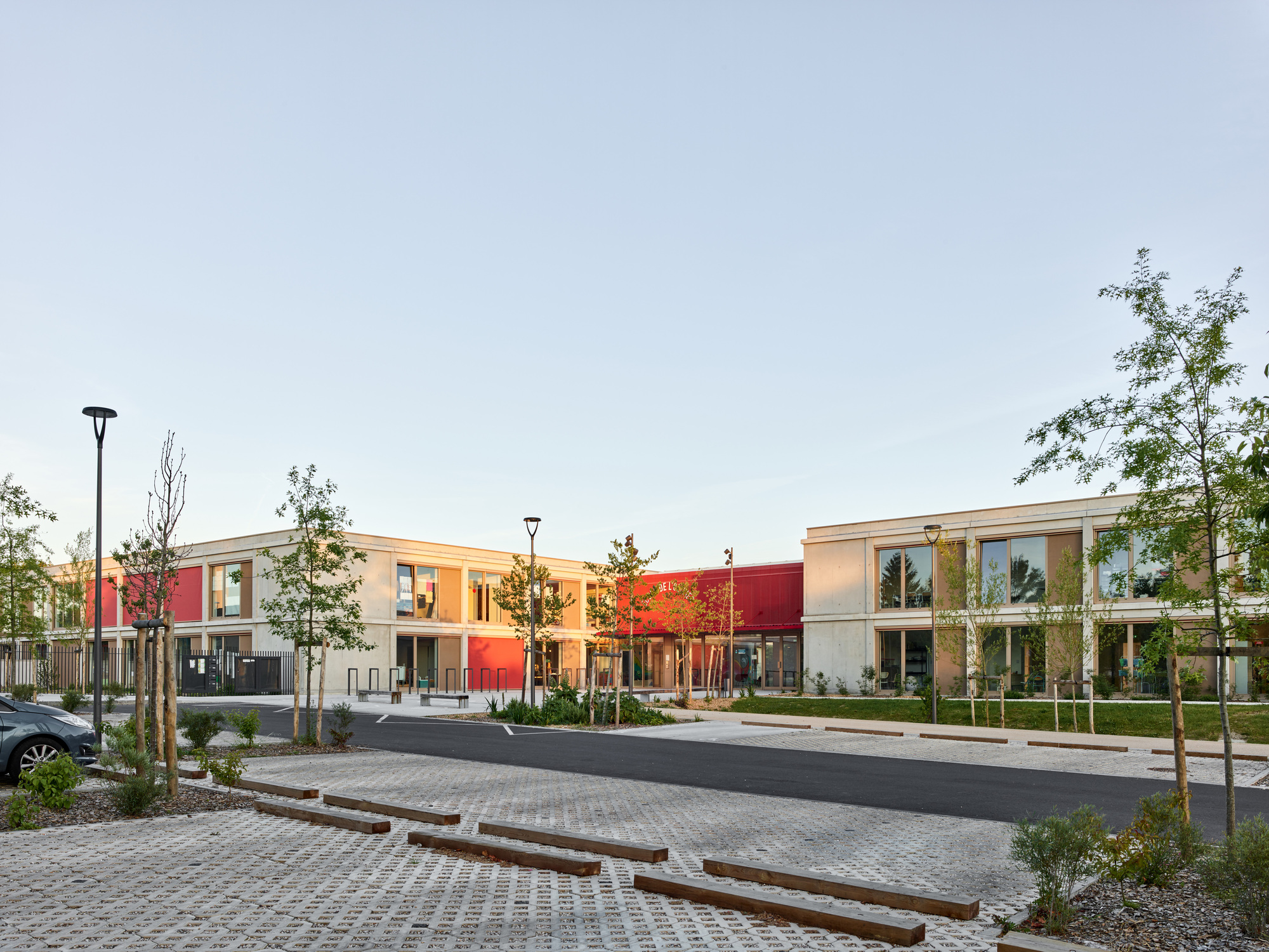 Street view of the school complex with planted beds and young trees at golden hour