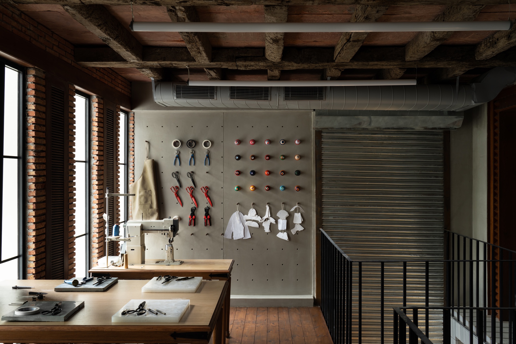 Upper level workspace with exposed timber beams, pegboard product wall, and louvered windows casting morning light