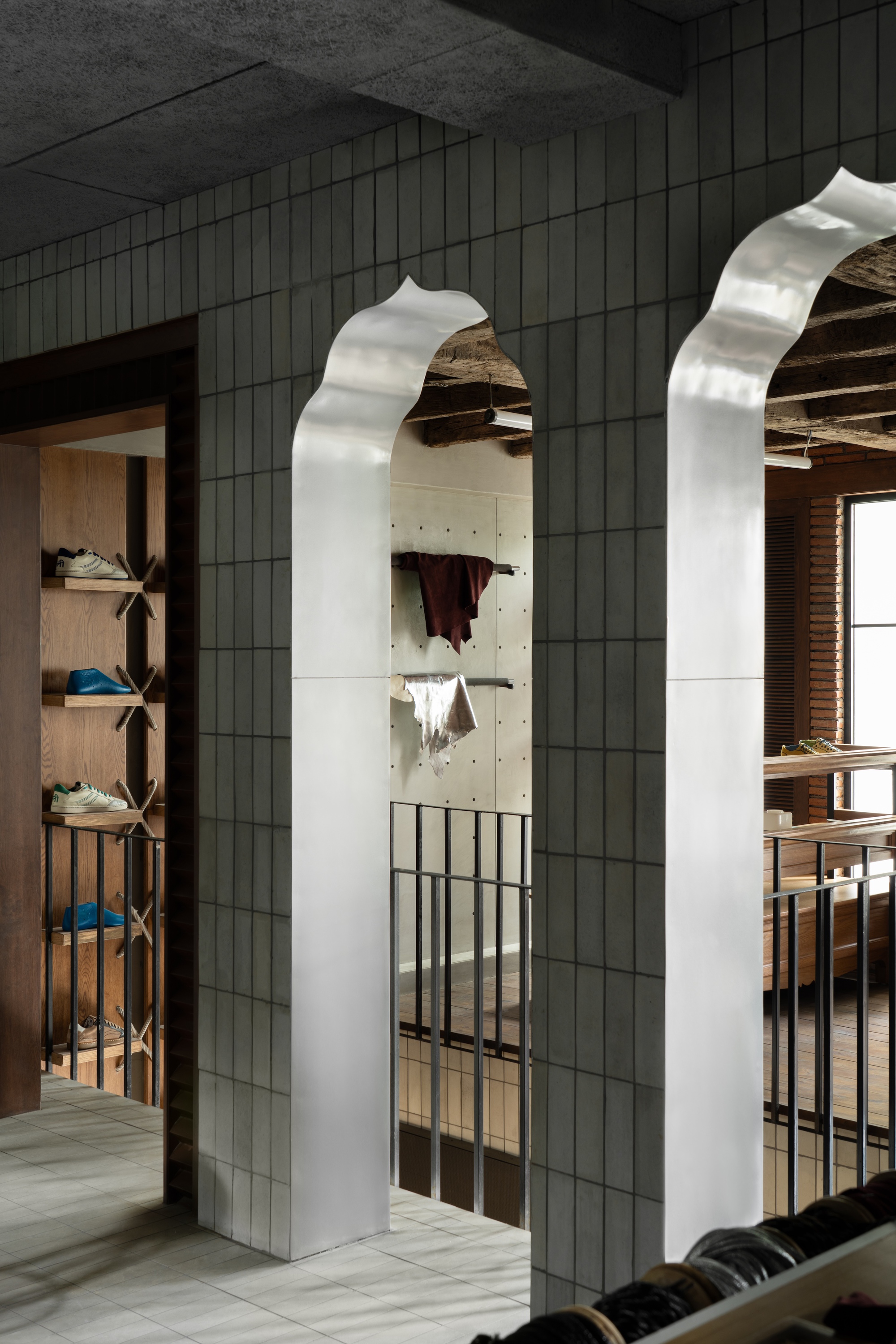 White ribbed portal columns framing arched openings through grey tile walls under reclaimed wood ceiling