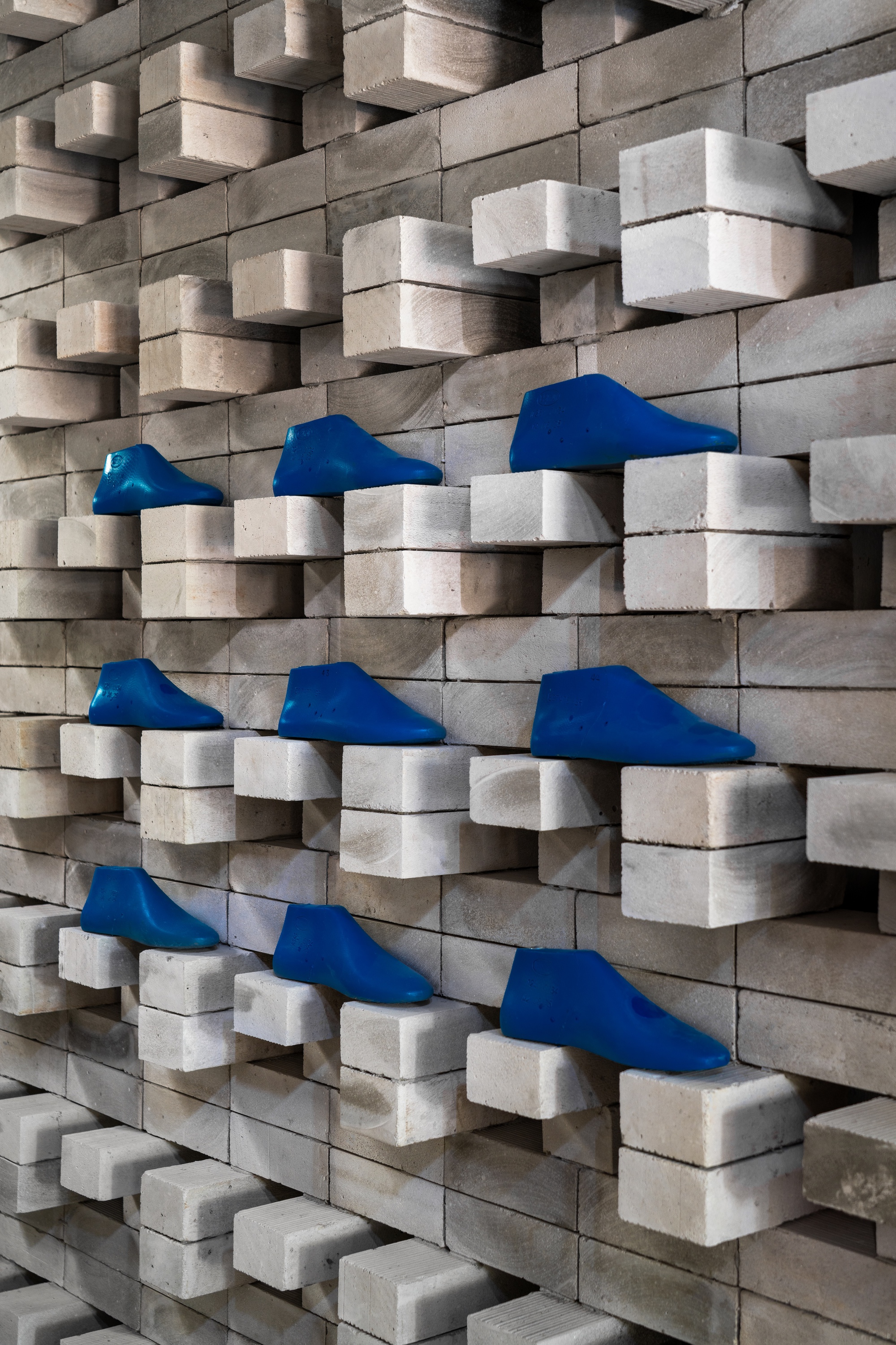 Close-up of staggered wood block wall with blue fabric footwear displayed on recessed ledges