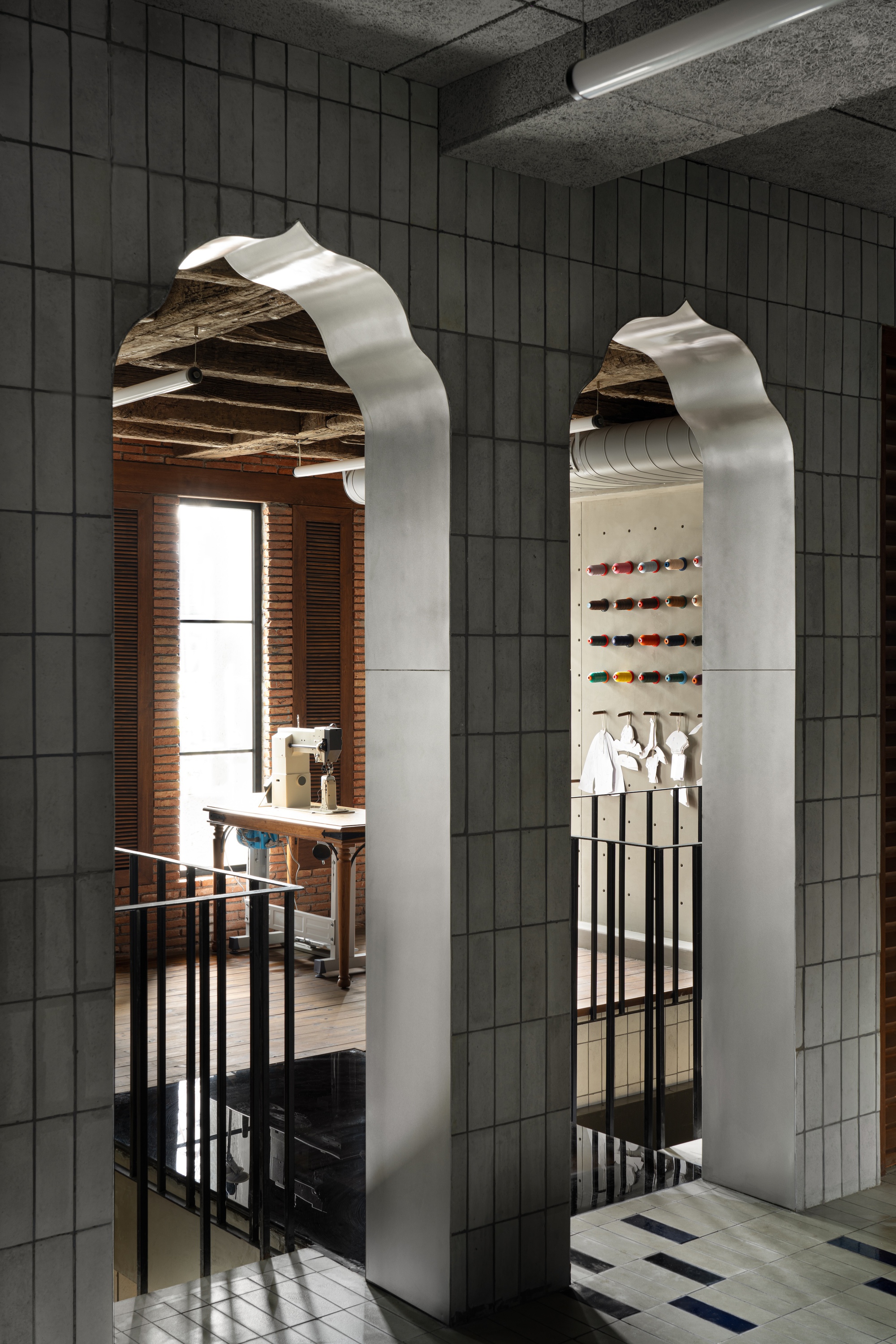 Two arched openings framed in white metal reveal a workspace with exposed timber beams and pegboard display