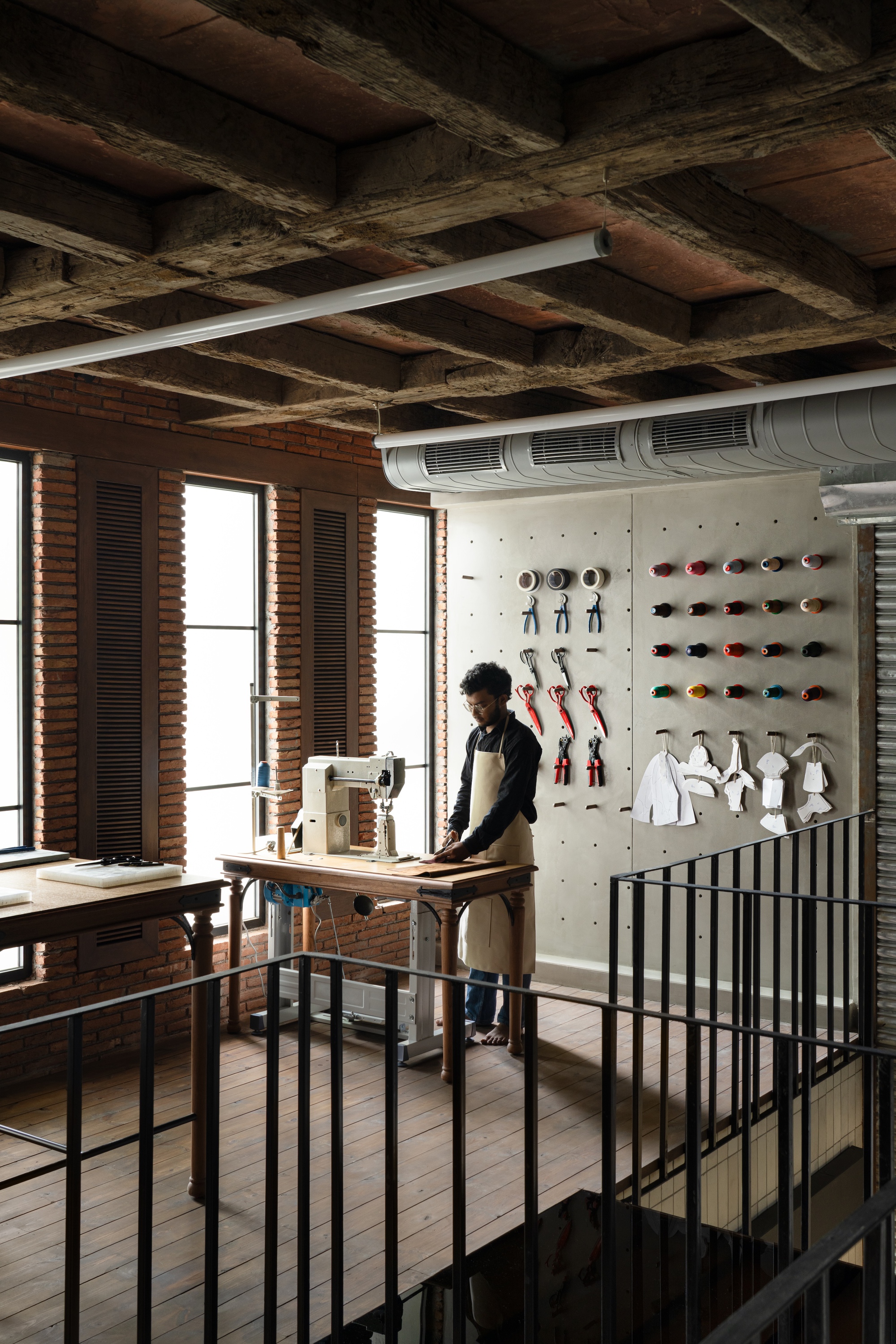 Upper level workspace with exposed timber ceiling joists and a person working at a cutting table