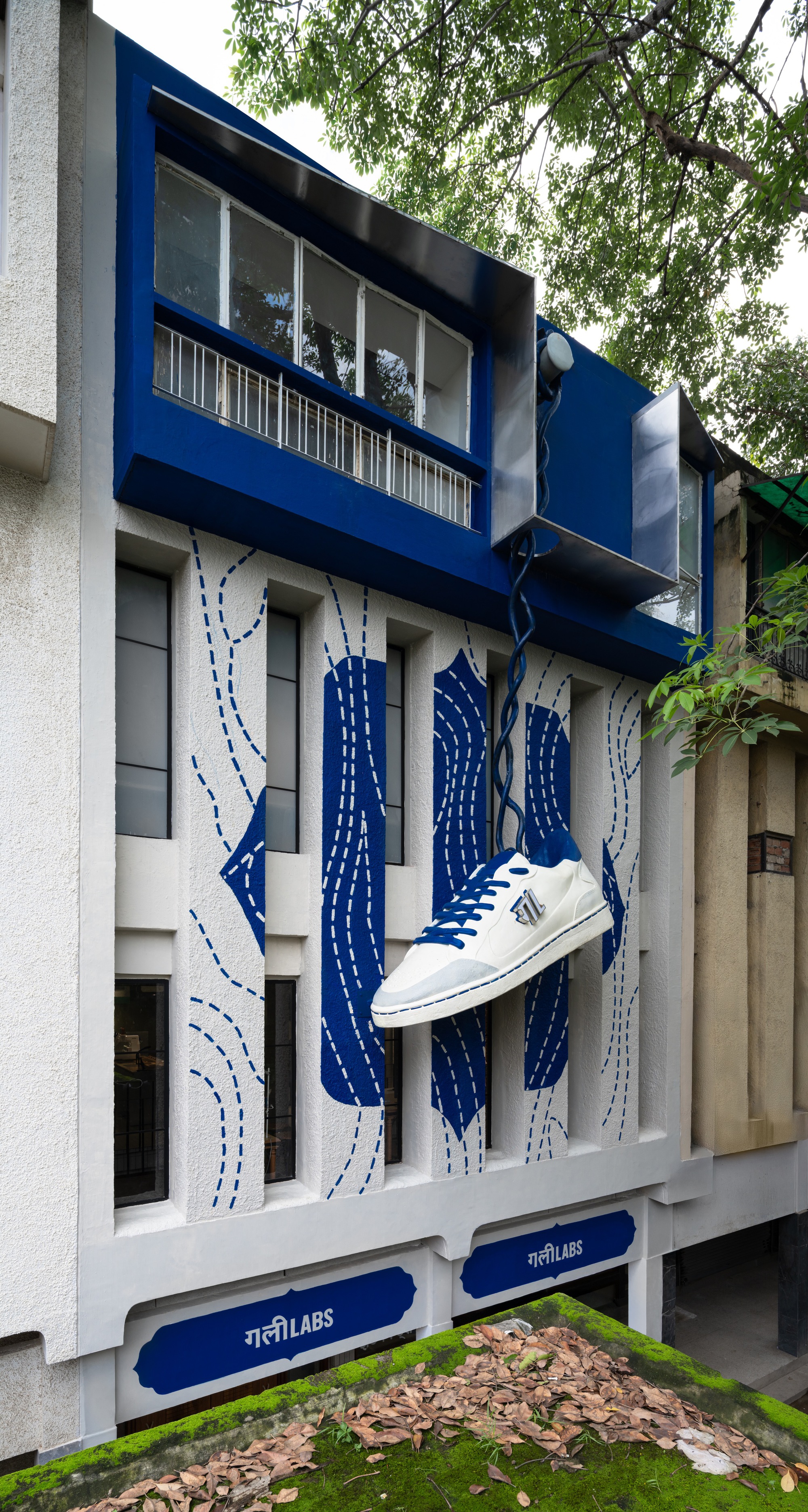 Street facade with blue frame and white sneaker sculpture suspended above blue and white stitch-pattern mural