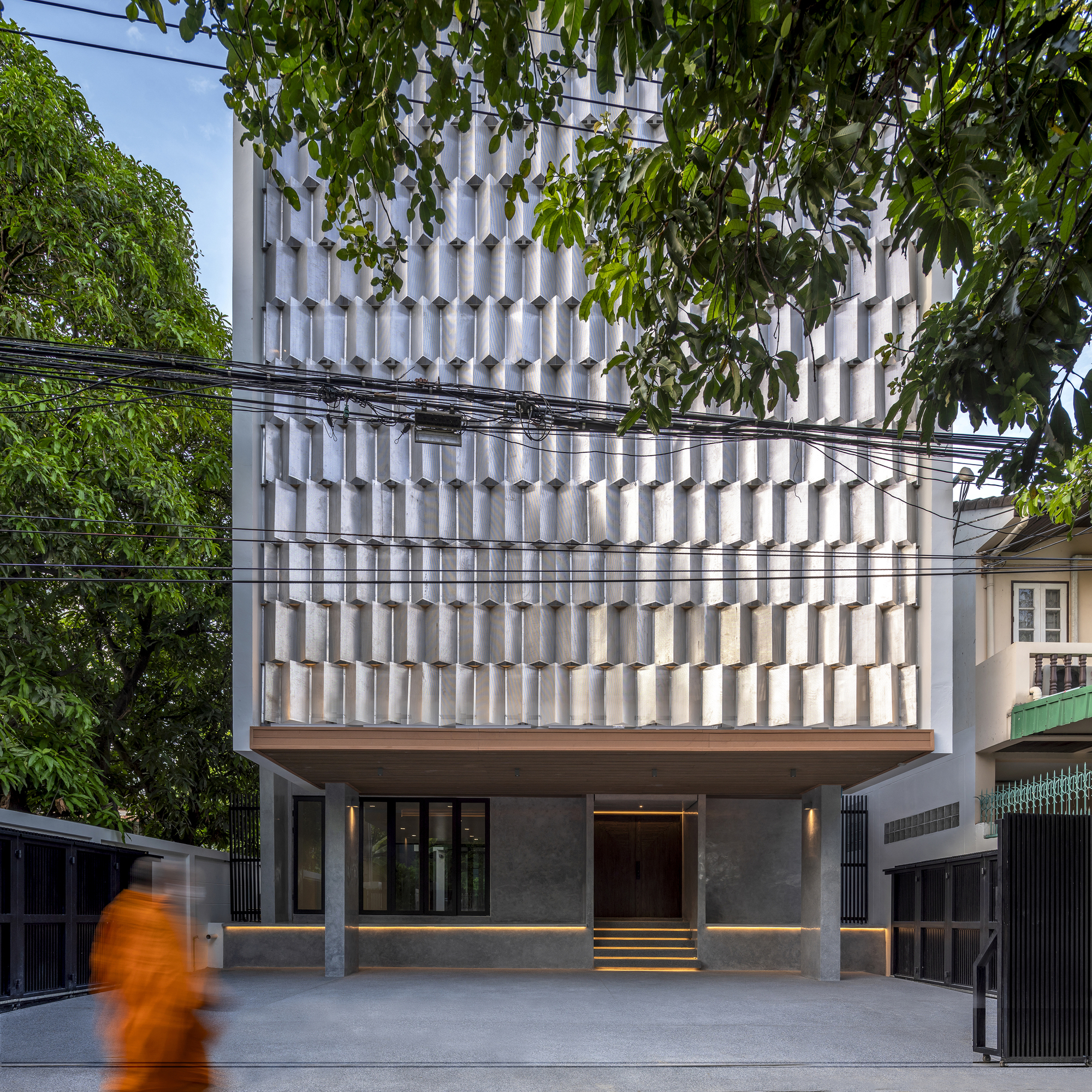 Street view of the white textured facade with overhead power lines and a pedestrian in motion