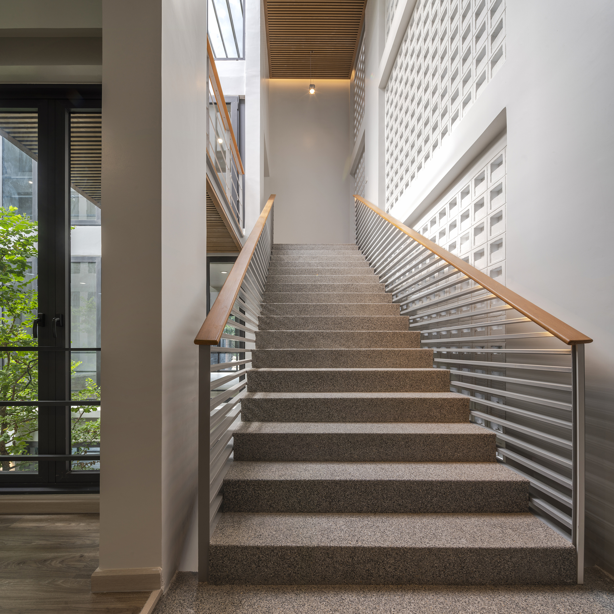 Terrazzo staircase with horizontal metal railings and timber handrails ascending toward a slatted timber ceiling