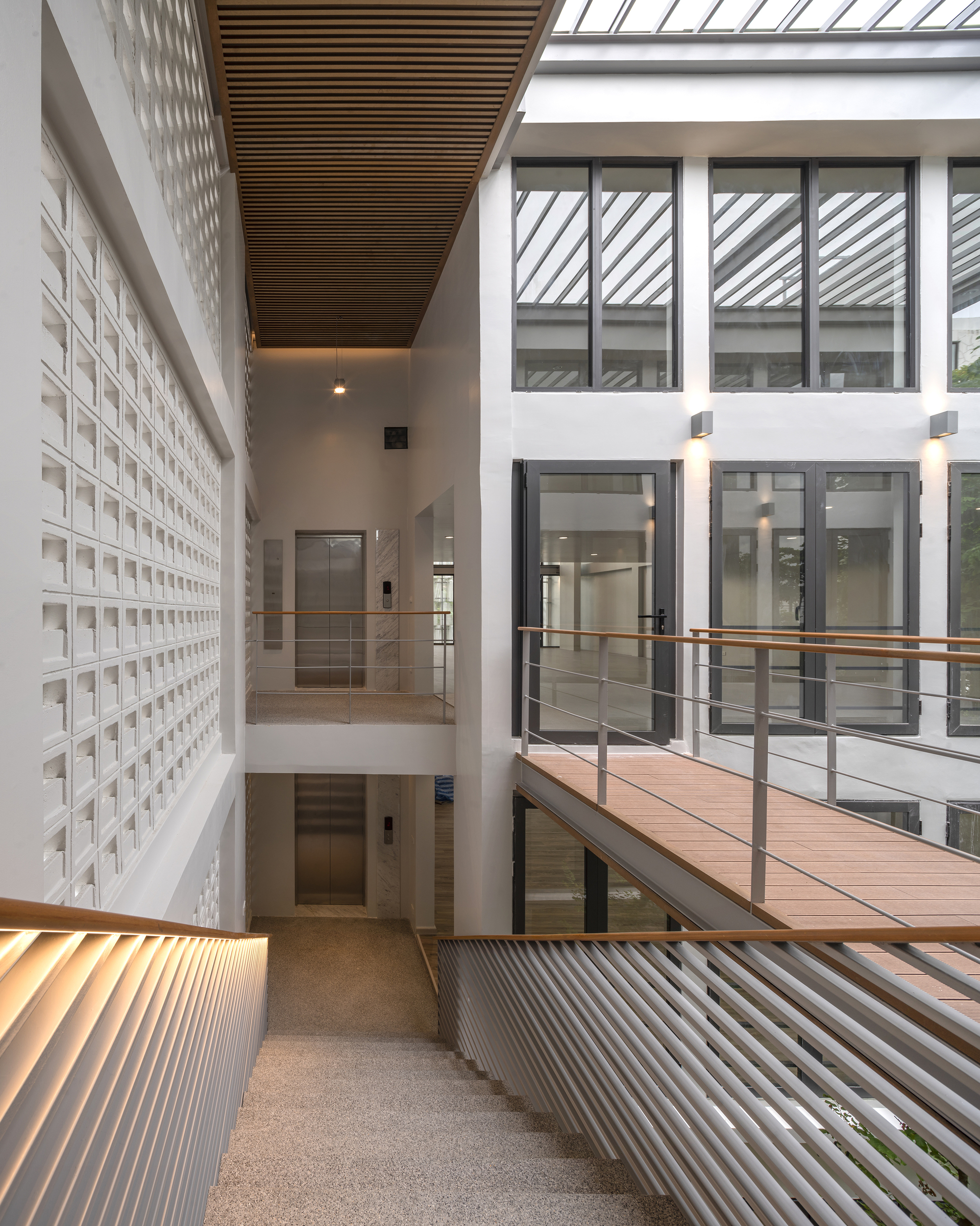 Upper level walkway with timber bridge connecting white perforated block walls under skylights