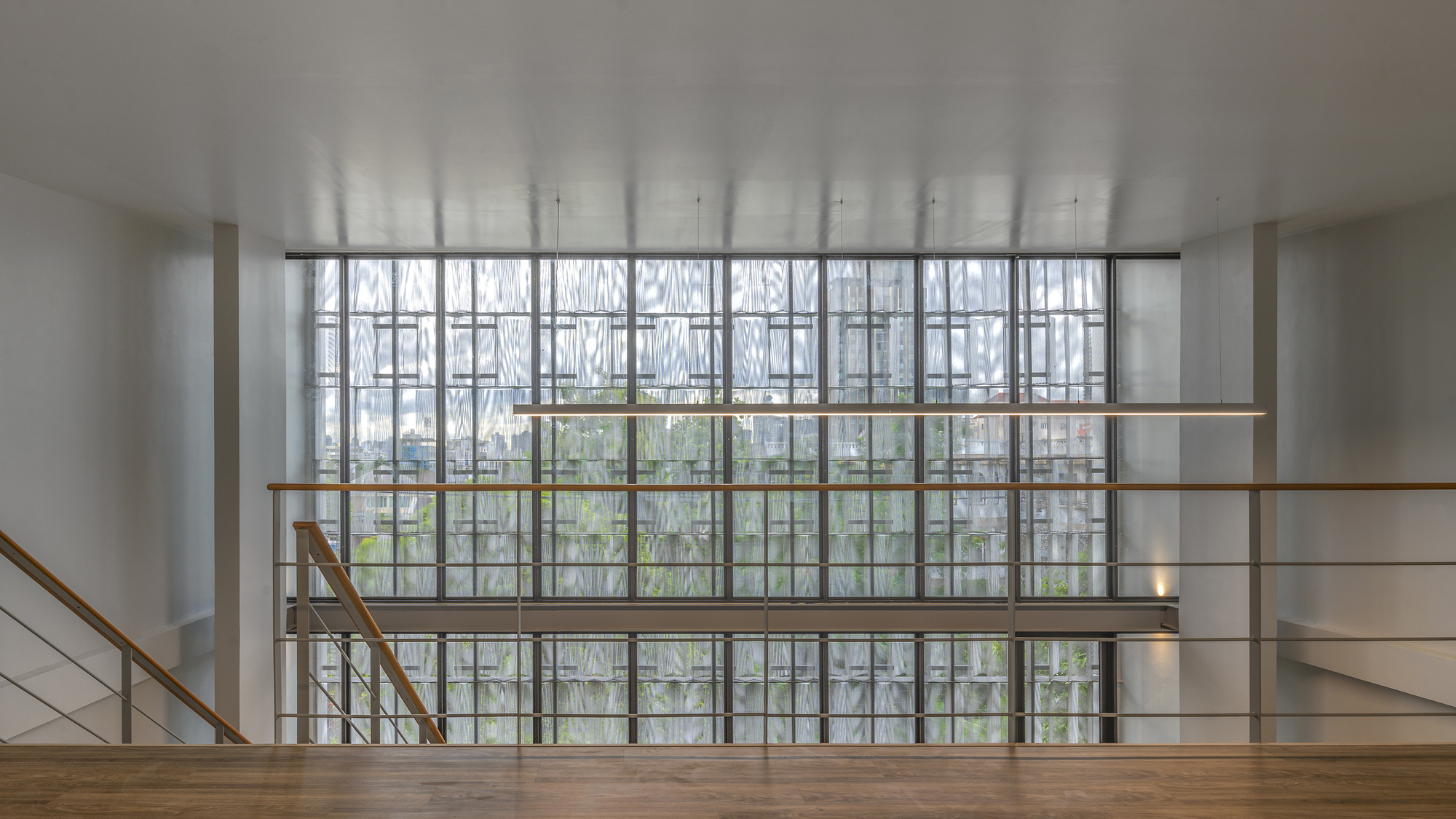 Interior stairwell landing facing gridded window wall with diagonal muntins and overcast daylight