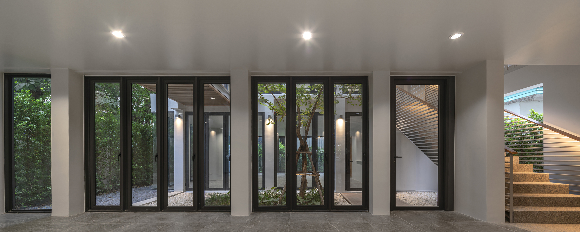 Interior room with black-framed glass doors opening to multiple planted courtyards at dusk
