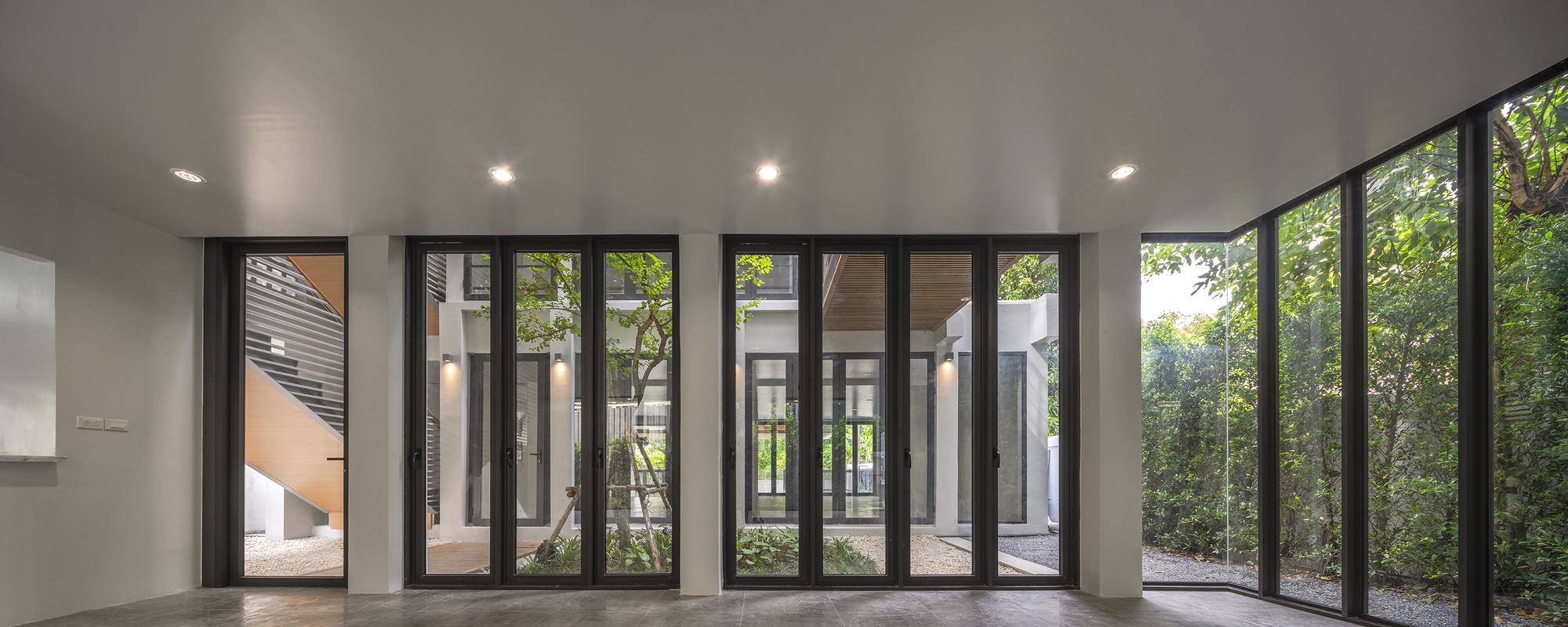 Interior space with folding glass doors surrounding courtyard gardens with mature trees