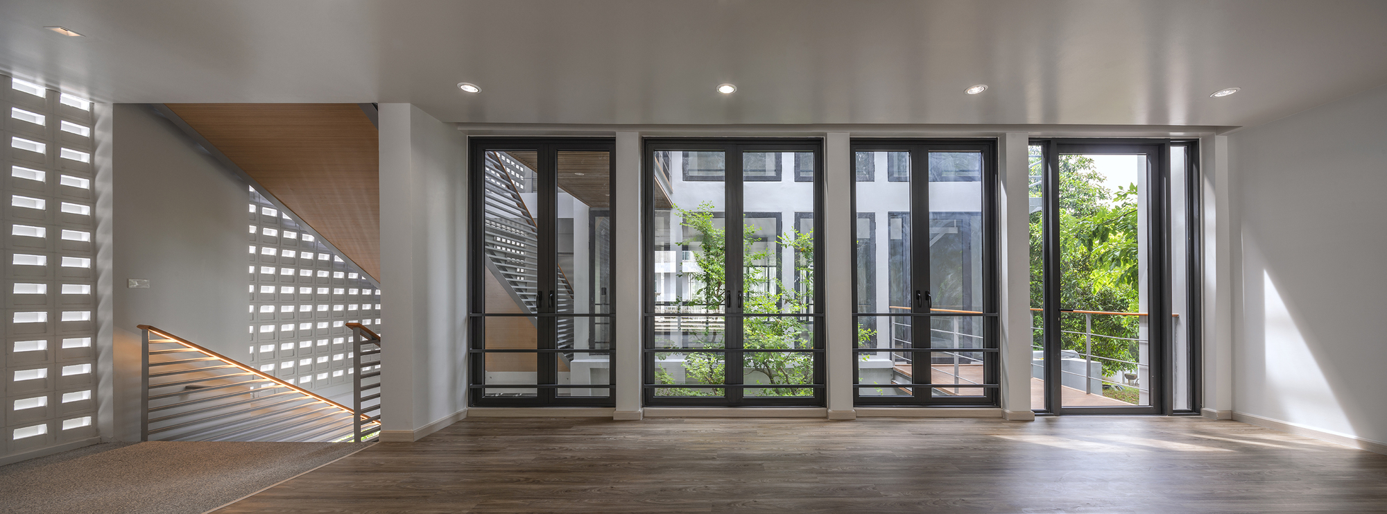 Interior room with timber flooring, glazed doors opening to a planted terrace, and a perforated screen wall filtering daylight