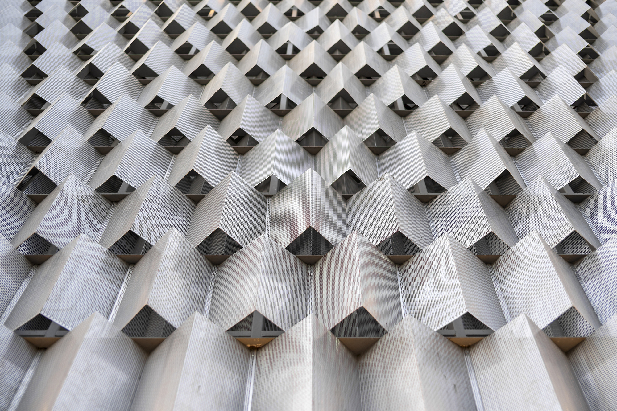 Close-up of textured concrete facade showing diamond-shaped projections with metal inserts creating a patterned surface