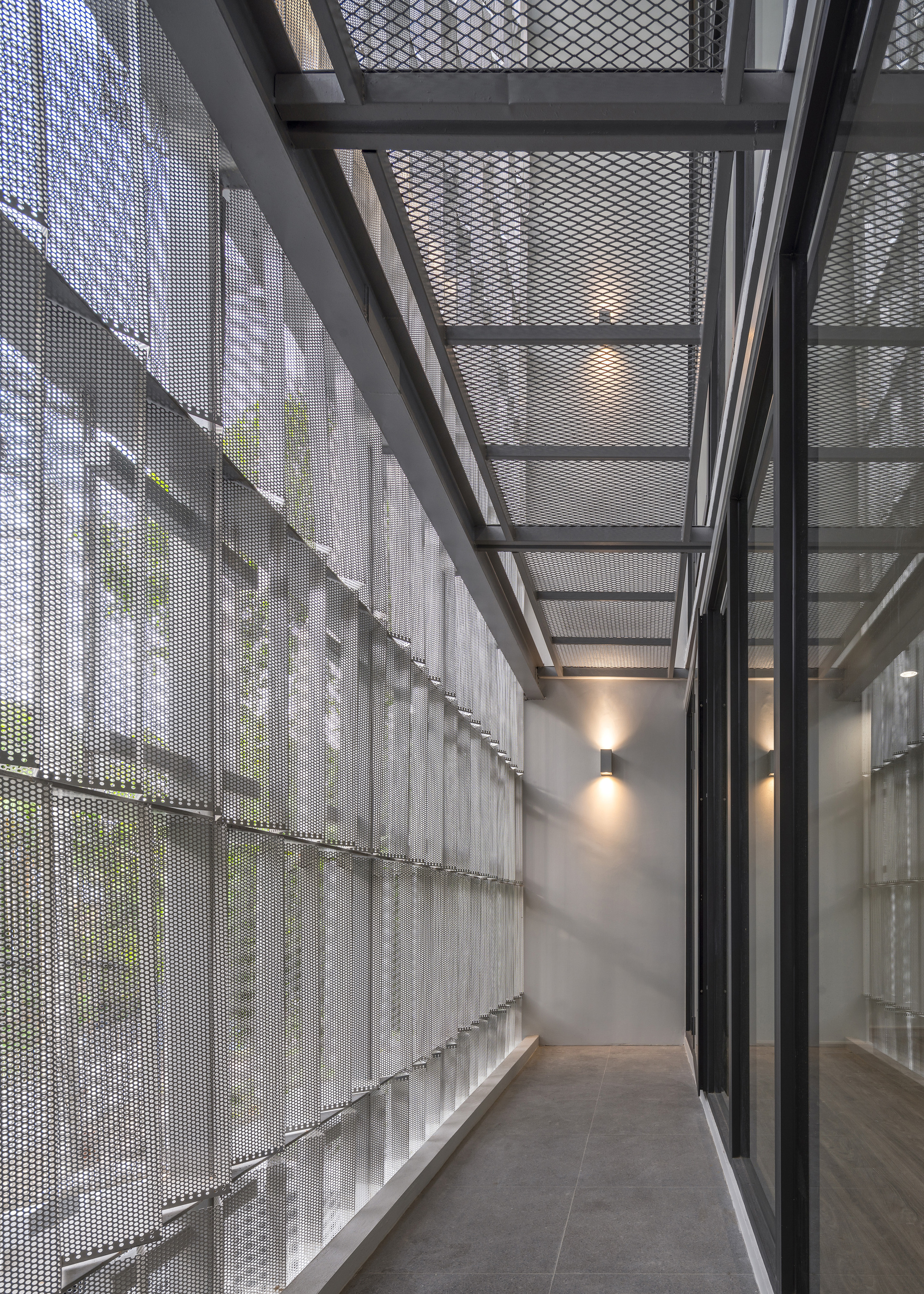 Narrow corridor with perforated metal screen wall and steel skylight structure overhead in diffused daylight