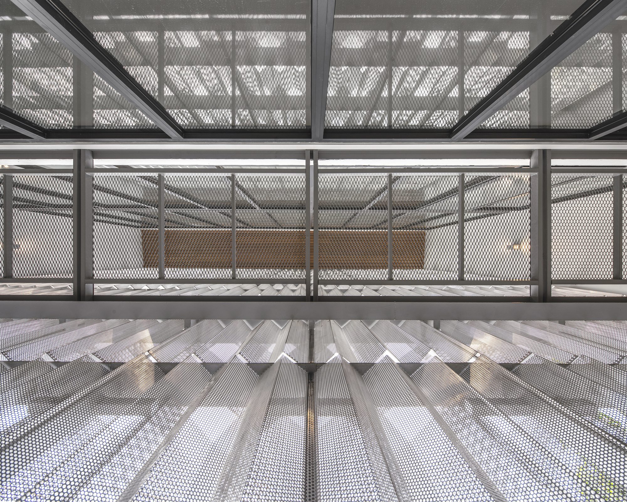 Looking up through stairwell clad in perforated metal mesh with zigzag folded underside