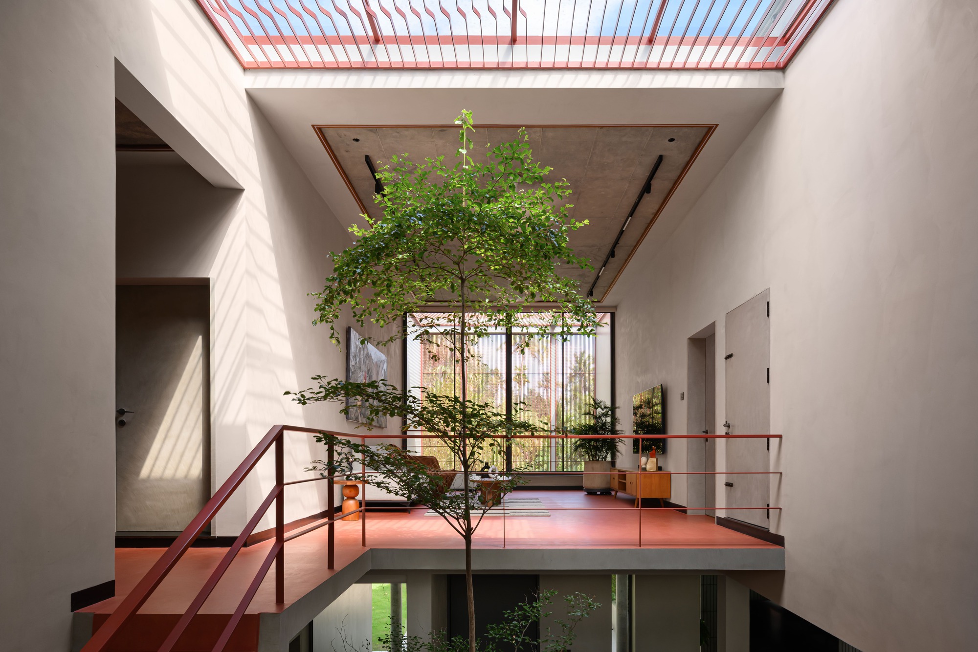 Double height interior courtyard with tree growing through red platform and striped skylight above