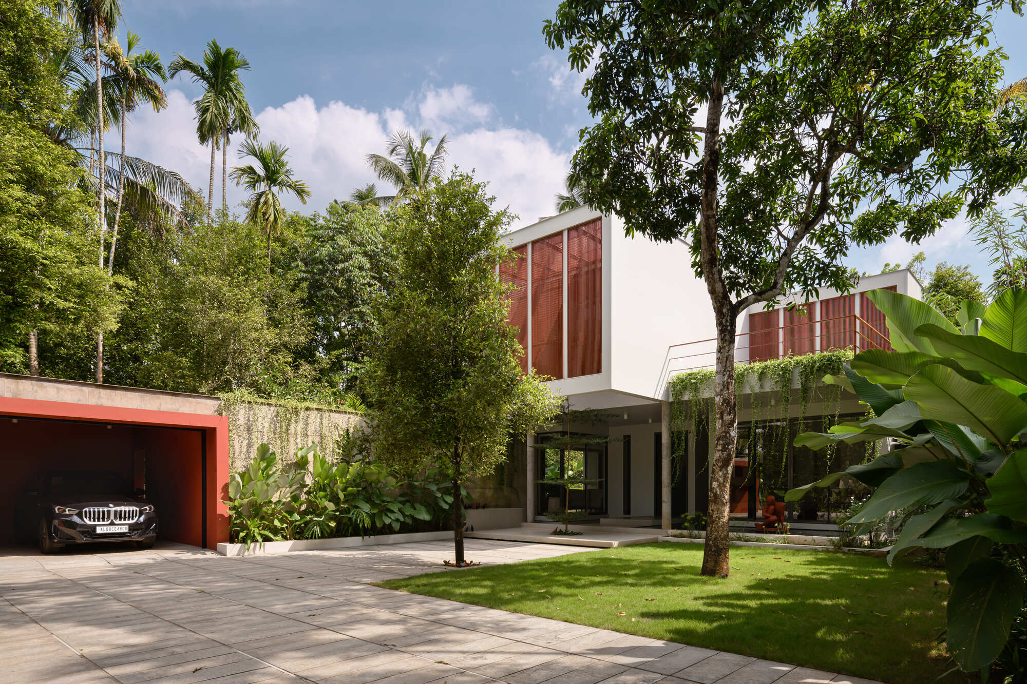 Street view showing piloti ground floor with red screened upper volumes among palms and lawn