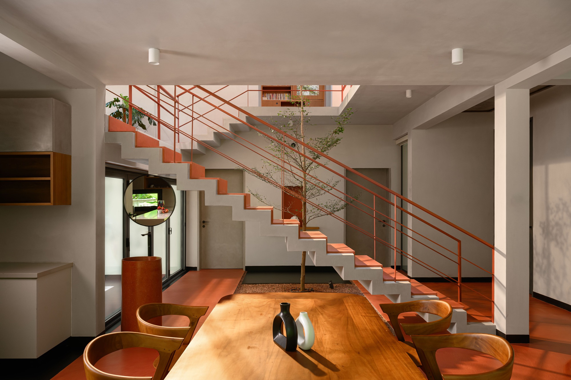 Double-height living space with orange-trimmed concrete staircase and metal railing under natural light
