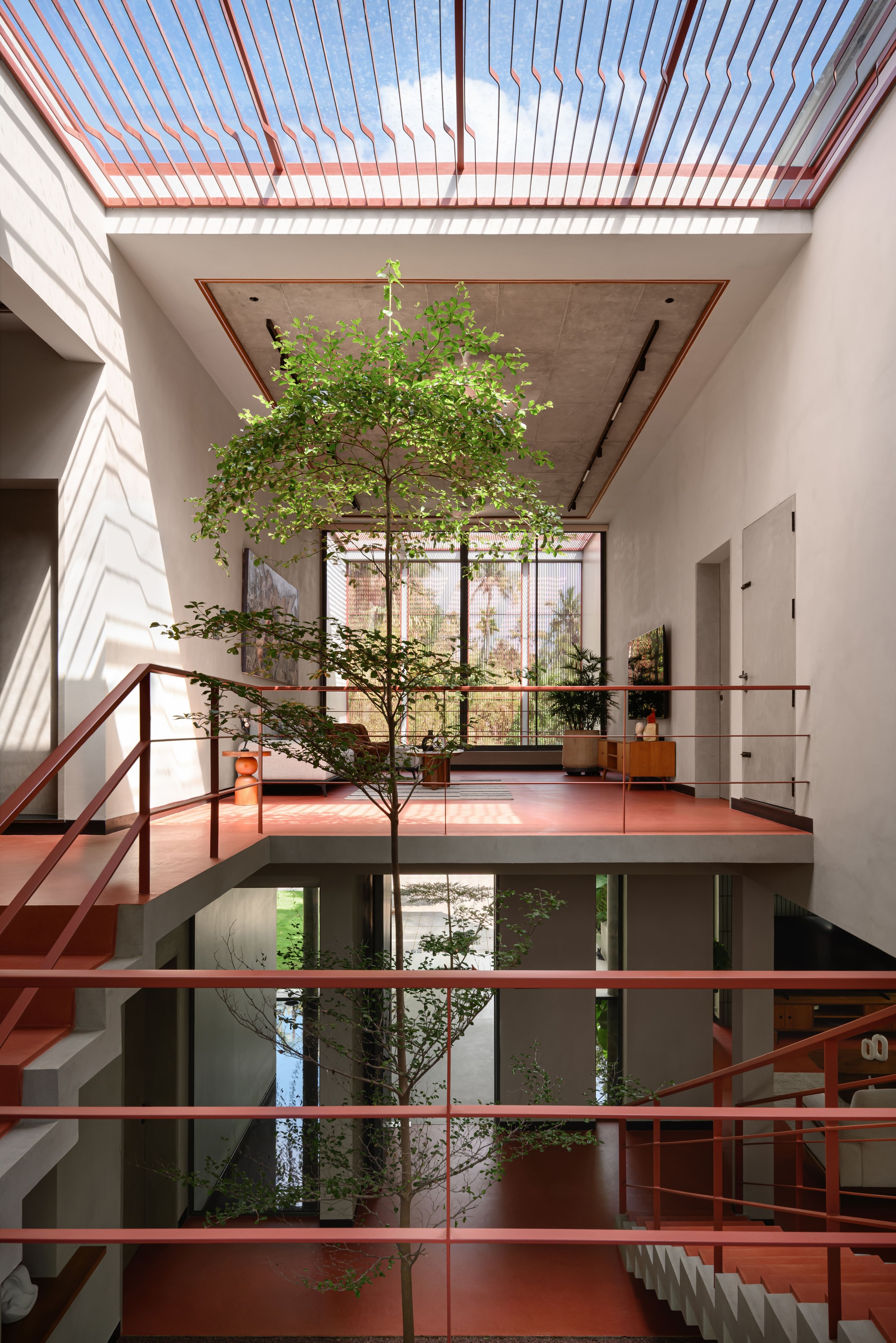 Central atrium with tree growing through floors under a slatted skylight with orange framing