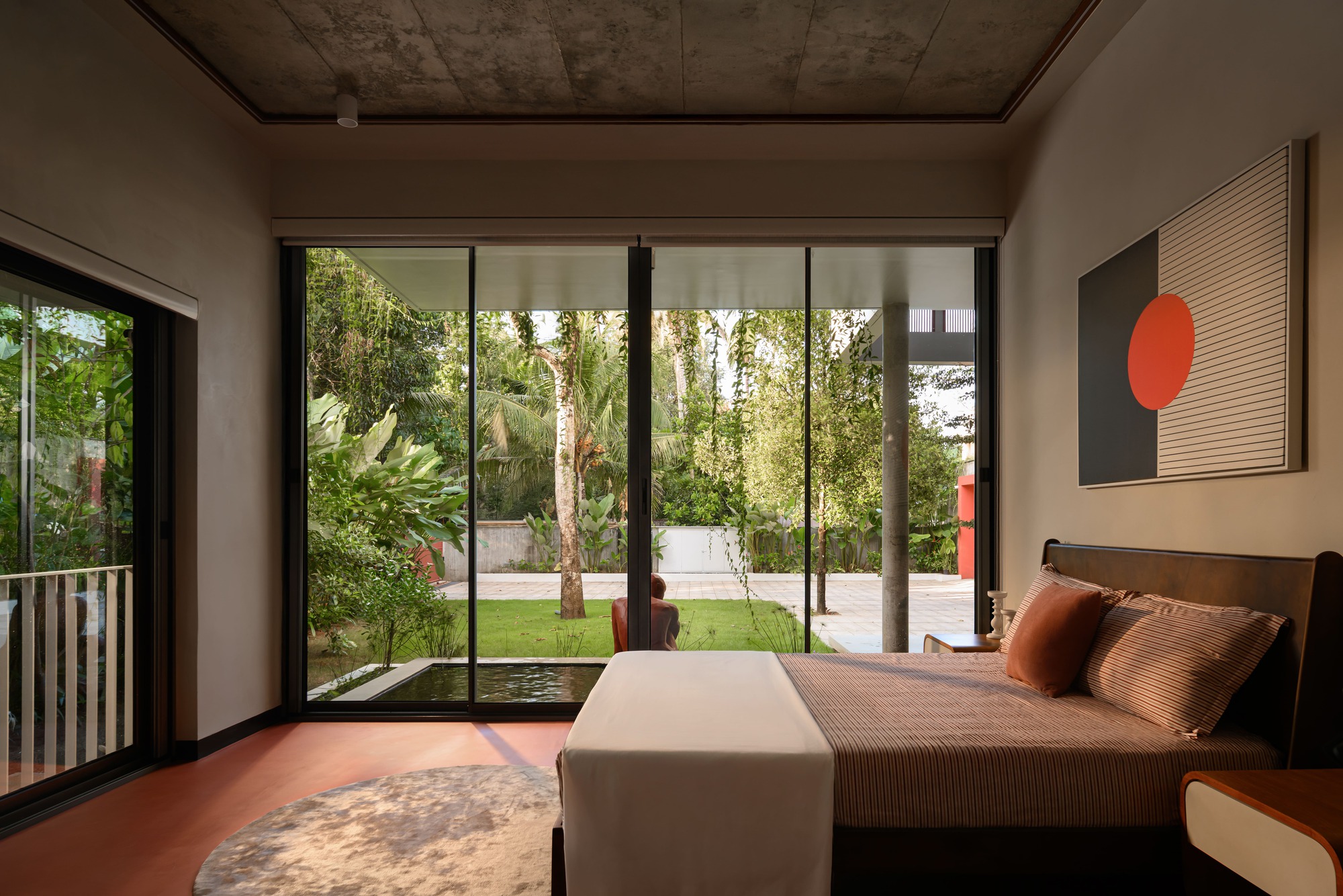 Bedroom with exposed concrete ceiling and floor-to-ceiling glazing opening to a grassed courtyard with birch trees