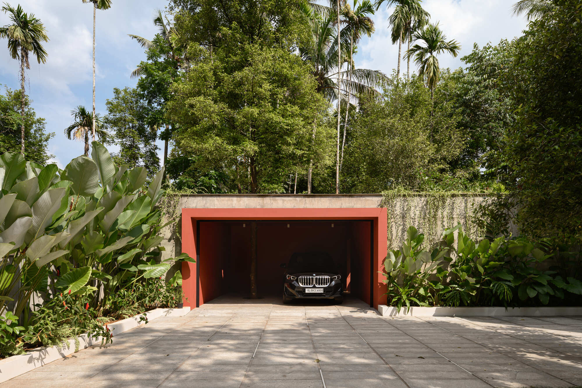 Recessed garage with coral-painted frame set into a concrete retaining wall surrounded by palms and tropical planting
