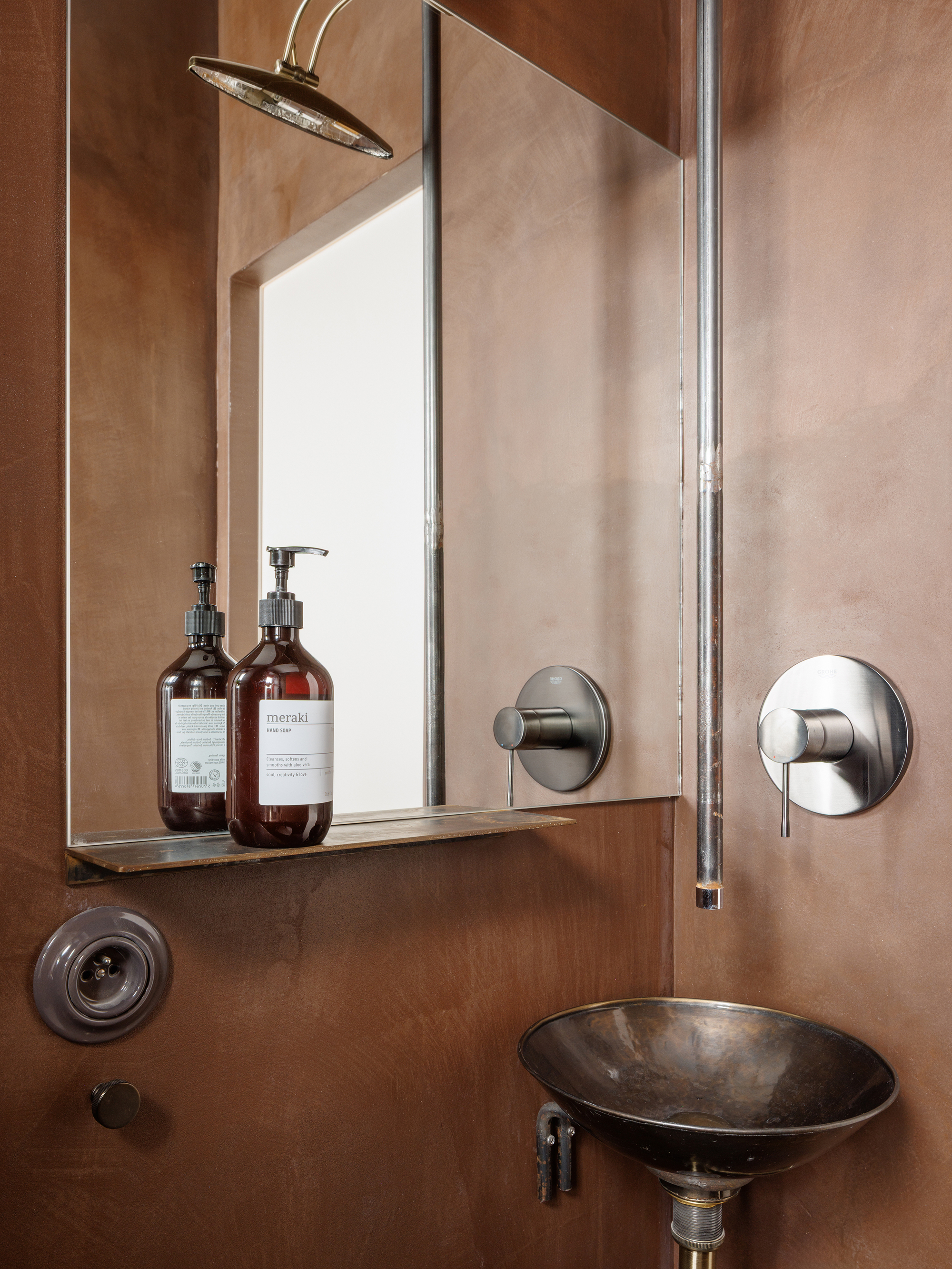 Bathroom corner with bronze vessel sink, mirror shelf with glass bottles, and brass rainfall showerhead