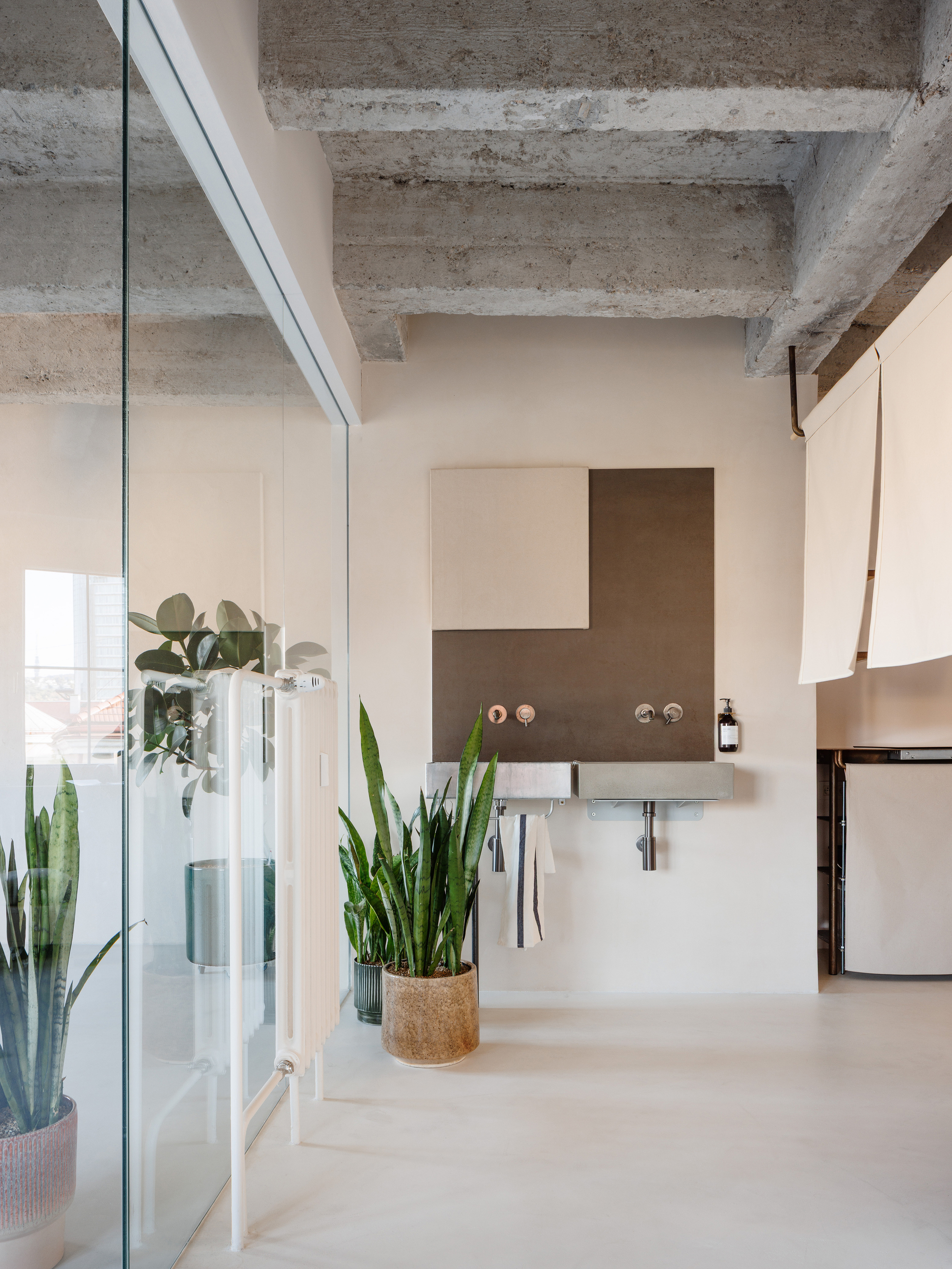 Open loft space with wall-mounted sink, geometric backsplash panel, potted plants, and concrete ceiling