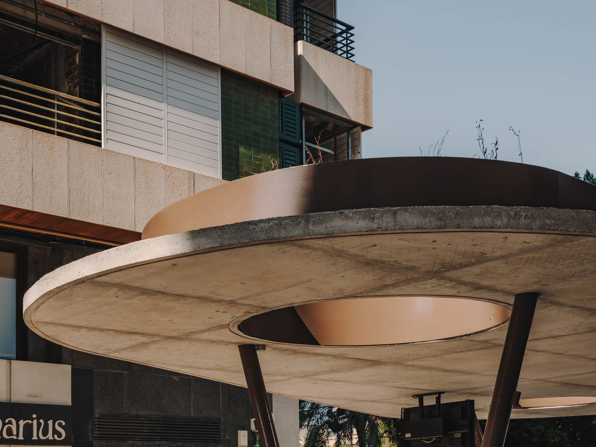 Underside detail of concrete canopy showing circular oculus and corten steel edging against overcast sky