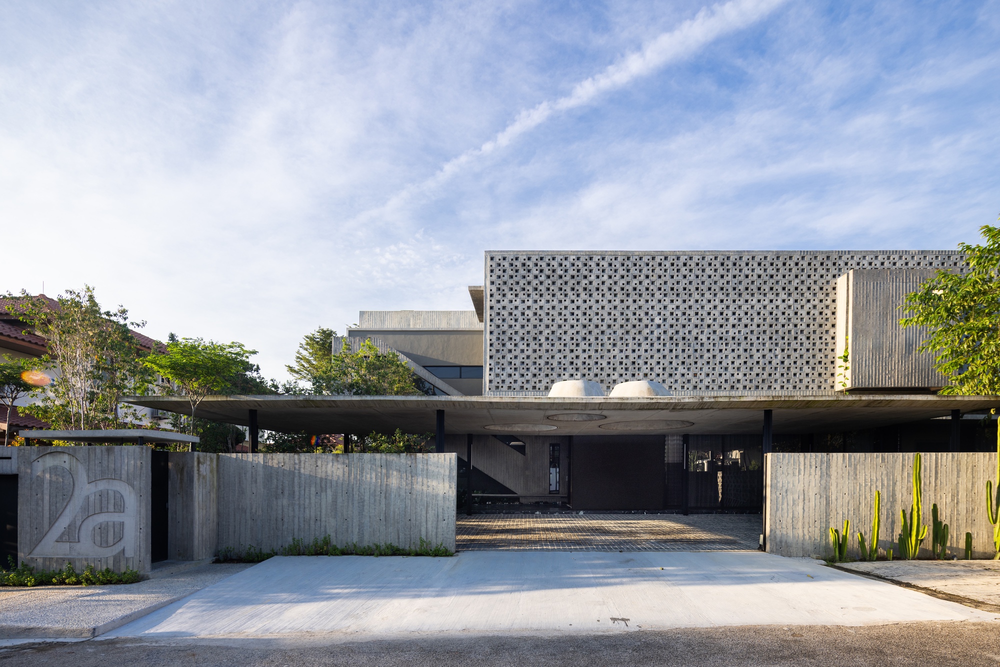 Street view of the perforated concrete screen facade above a cantilevered carport and board-formed concrete wall