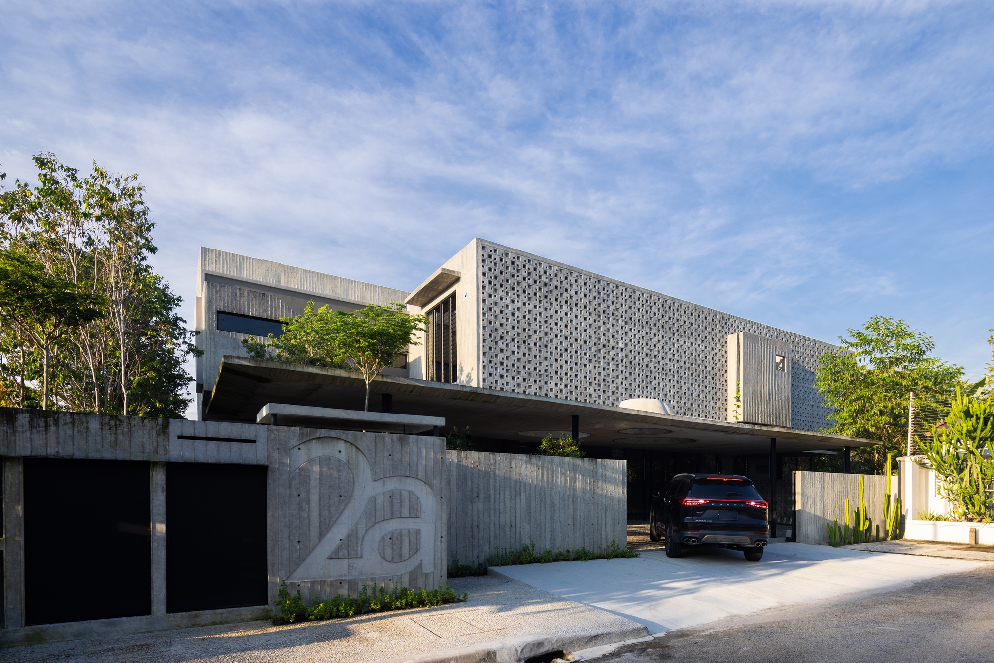 Facade showing the layered volumes with patterned concrete screen, timber cladding, and rooftop planting under blue sky