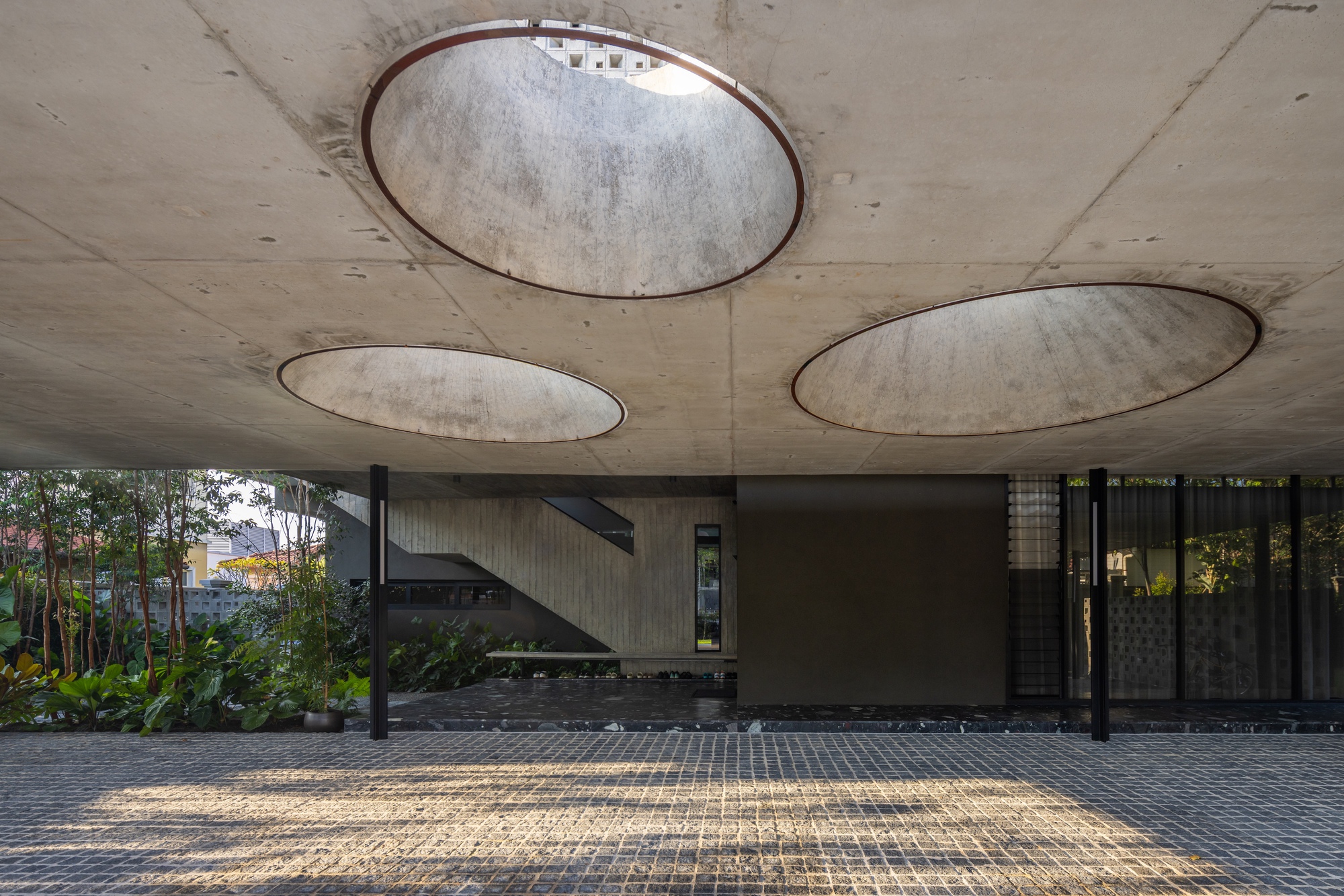 Covered carport with circular skylights cut into the board-formed concrete soffit above a paved driveway
