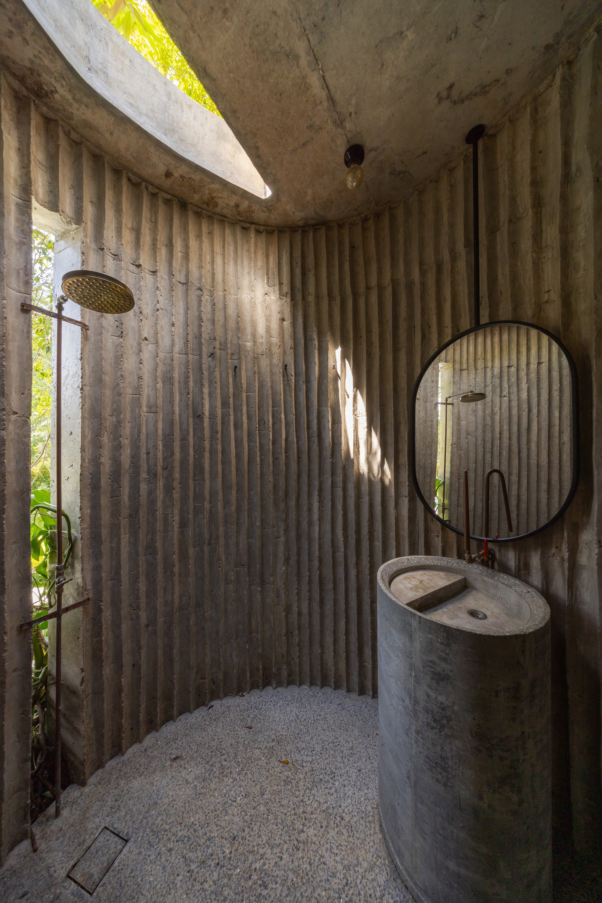 Curved bathroom enclosure with fluted concrete walls, circular sink, round mirror, and skylight casting morning light